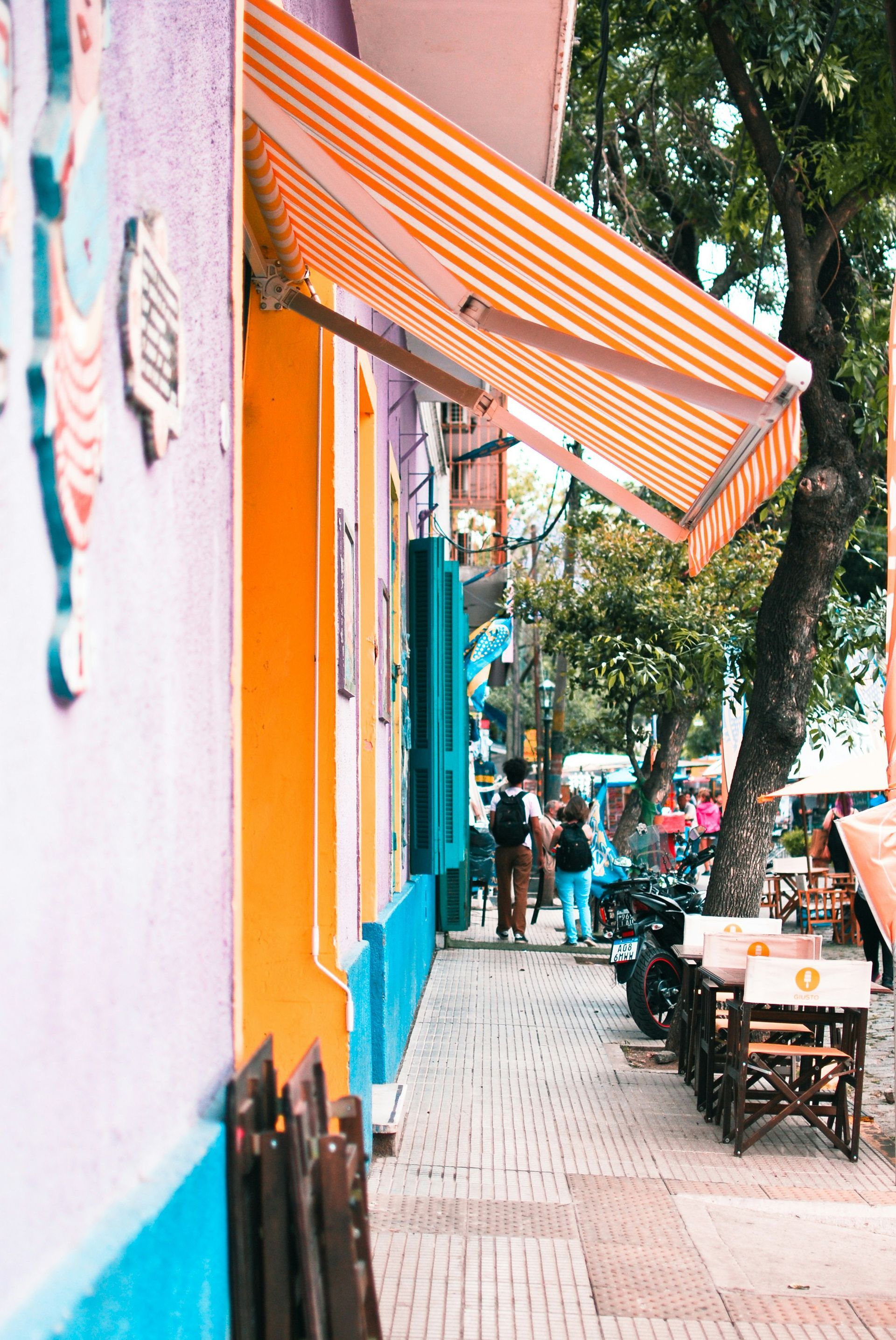 Colorful storefront with striped awning; people walking on the sidewalk in Buenos Aires, Argentina.