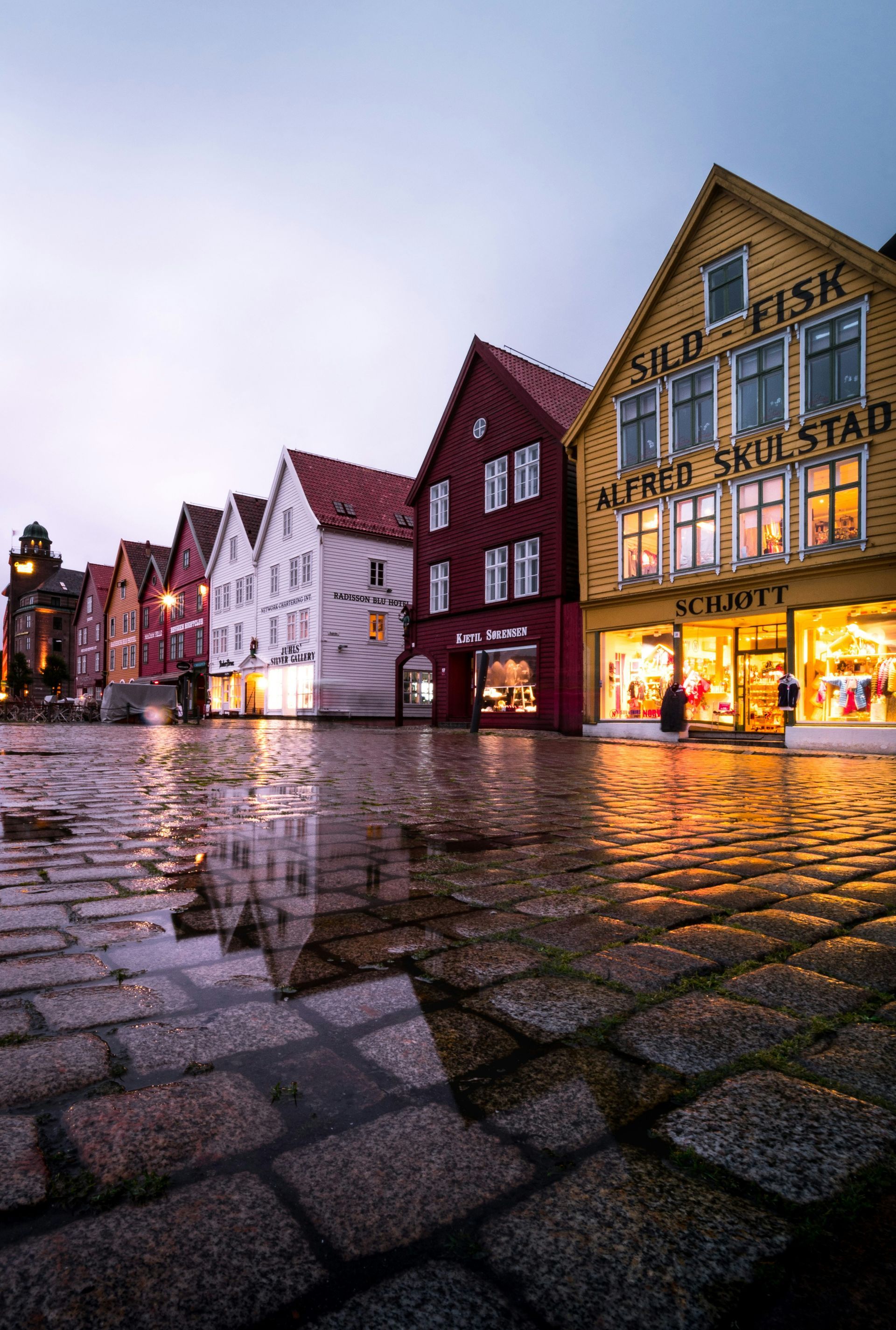 Colorful wooden buildings reflect in a wet cobblestone street in Bergen, Norway, after a rain.