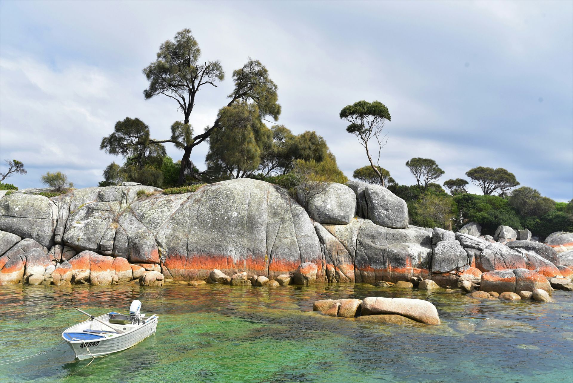 A small boat is sitting in the water near a rocky shoreline in Tasmania, Australia.