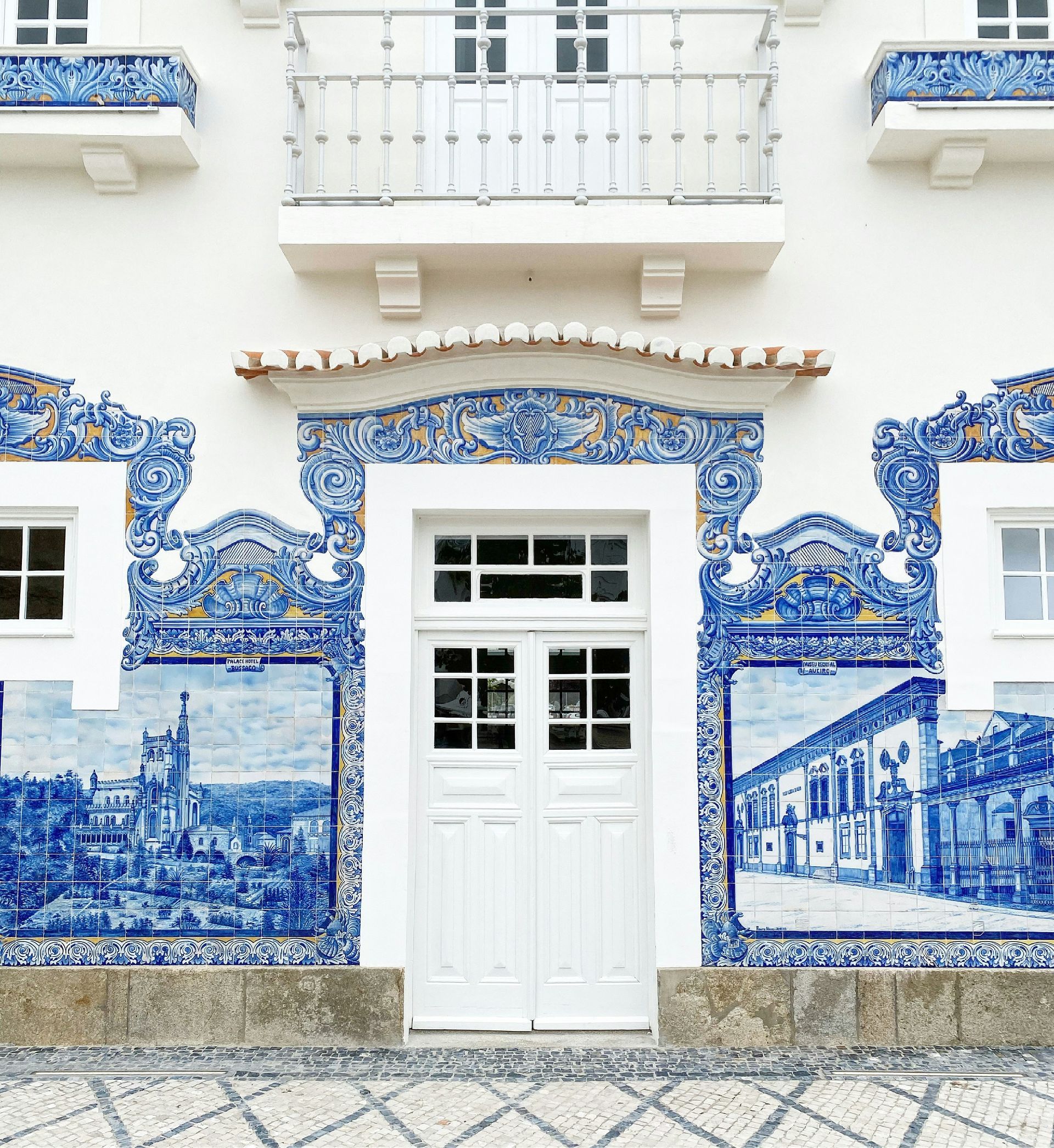 White door framed by blue and white tile murals on a building facade with a balcony above in Aveiro, Portugal.