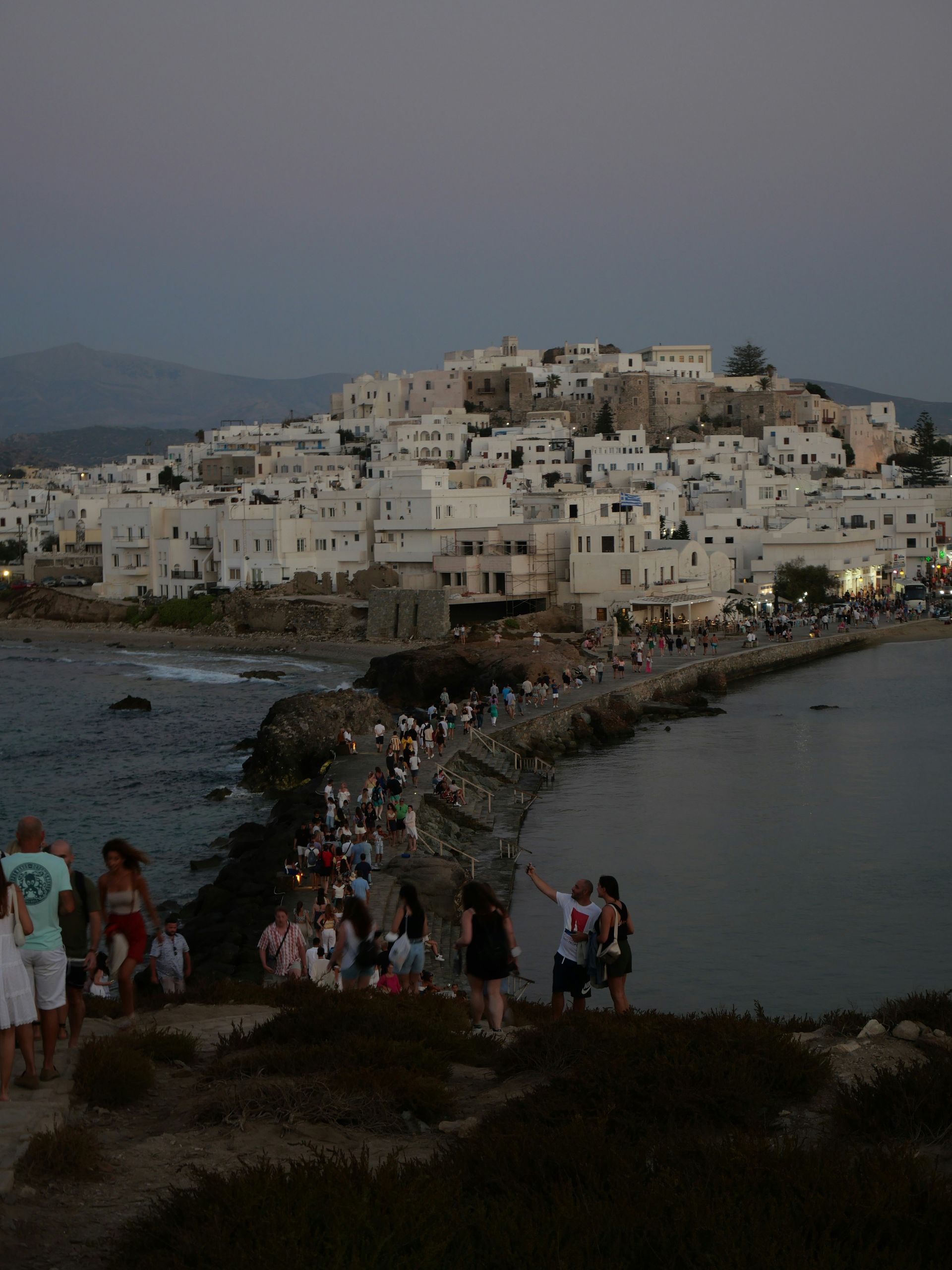 A group of people standing on top of a hill overlooking a body of water in Naxos, Greece.