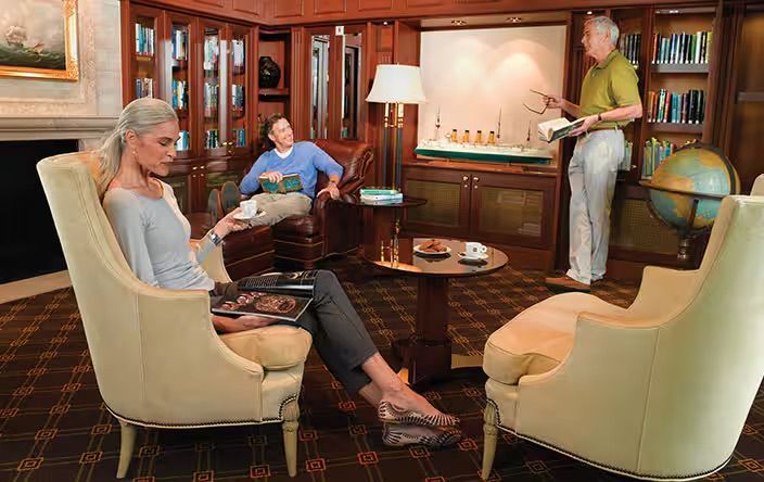 A group of people are sitting in chairs in a living room on the Oceania Riviera cruise ship.