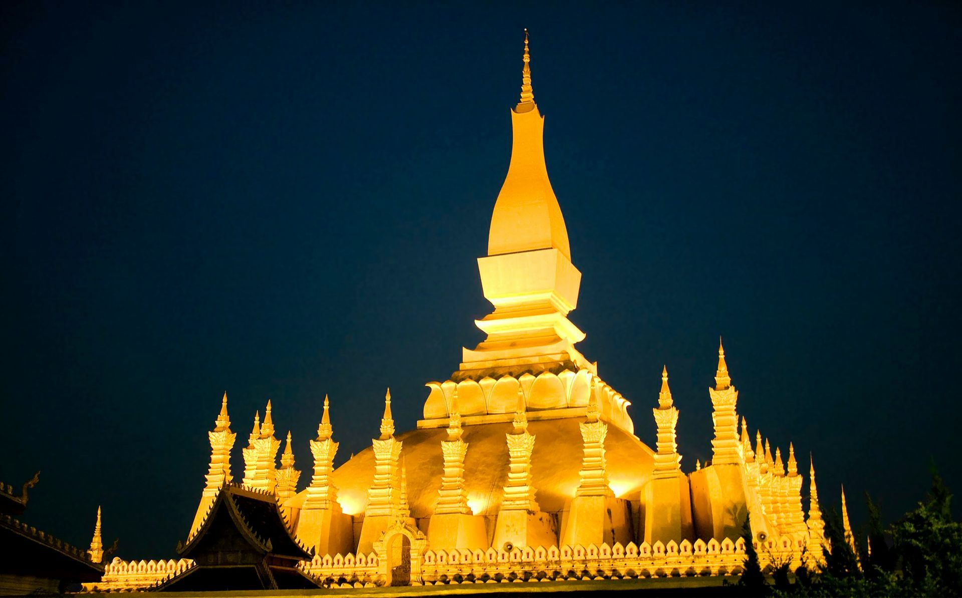 Illuminated golden Buddhist stupa against a dark blue night sky in Vientiane, Laos.