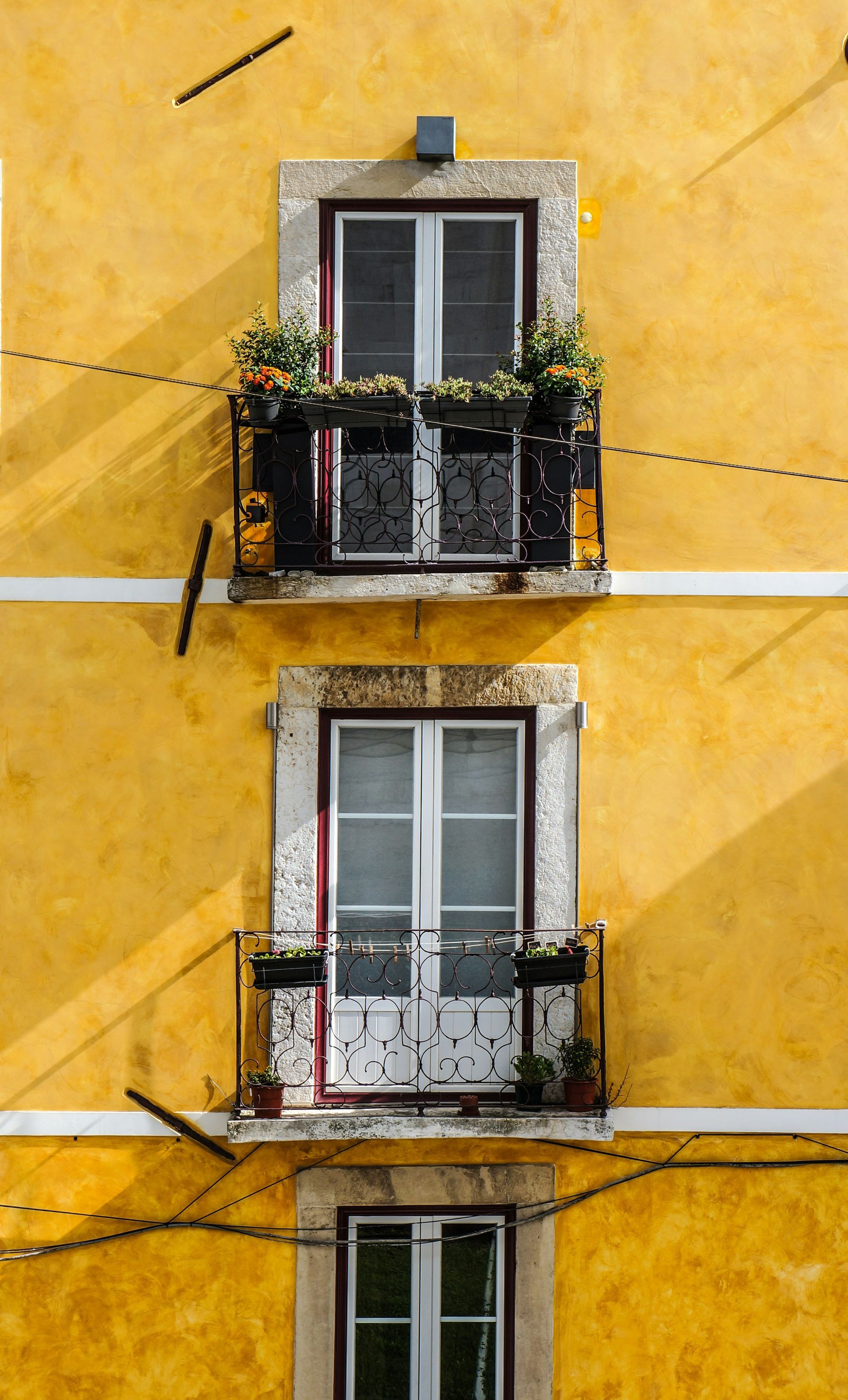 Yellow building with two balconies, each with window and flower boxes in Lisbon, Portugal.