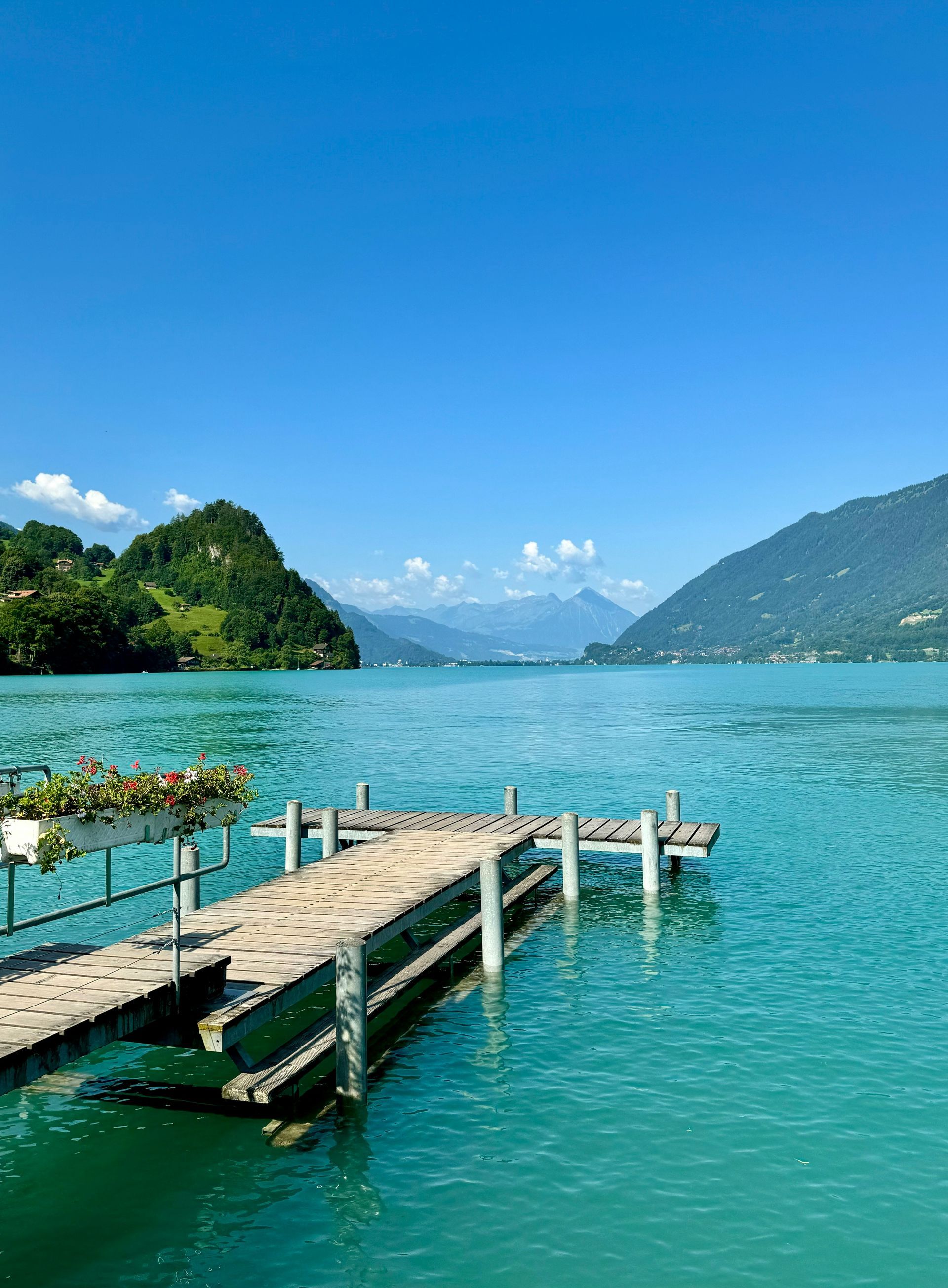 Wooden pier over turquoise water; mountains and blue sky in background in Interlaken, Switzerland.