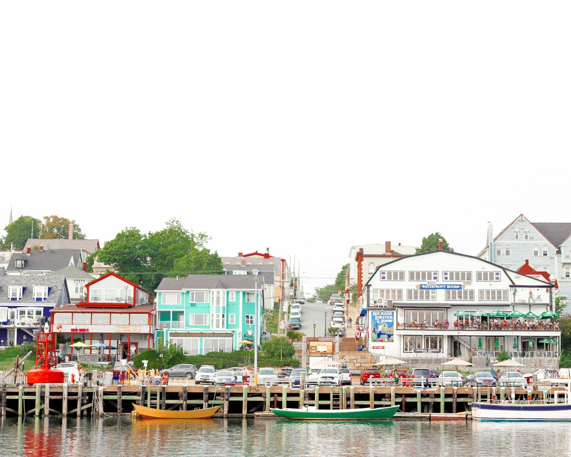 Waterfront view of a coastal town with colorful buildings, docks, and boats. A red buoy is visible in the foreground in Nova Scotia, Canada.