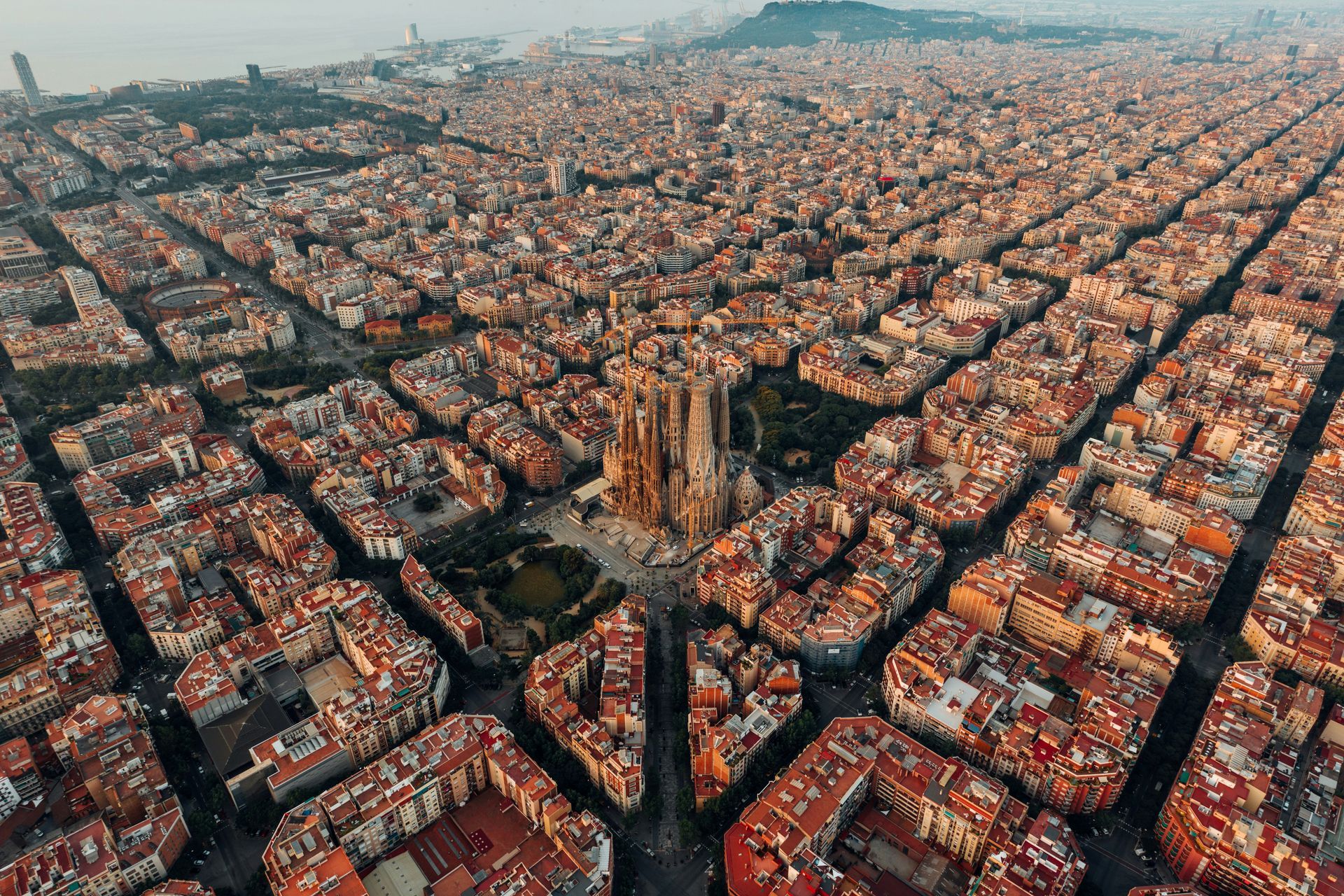 Aerial view of Barcelona, Spain, with the Sagrada Familia church at the center, surrounded by a grid of buildings.