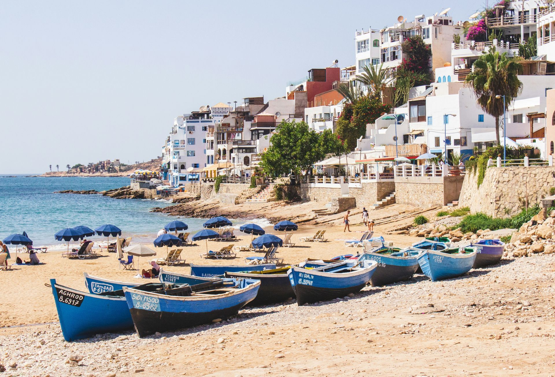 A row of blue boats are lined up on a beach in Taghazout, Morocco.
