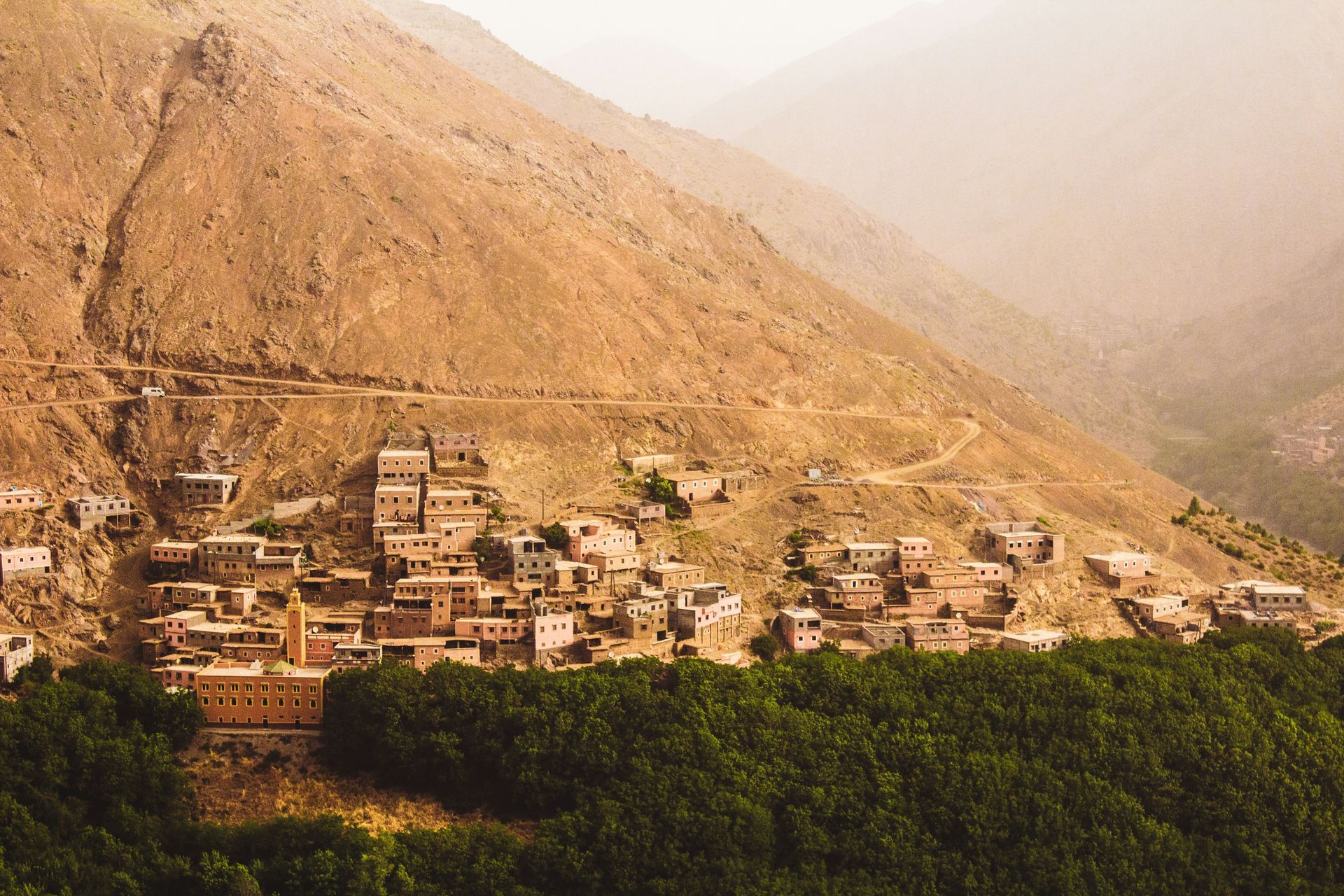 A small village is sitting on the side of a mountain surrounded by trees in Toubkal, Morocco.