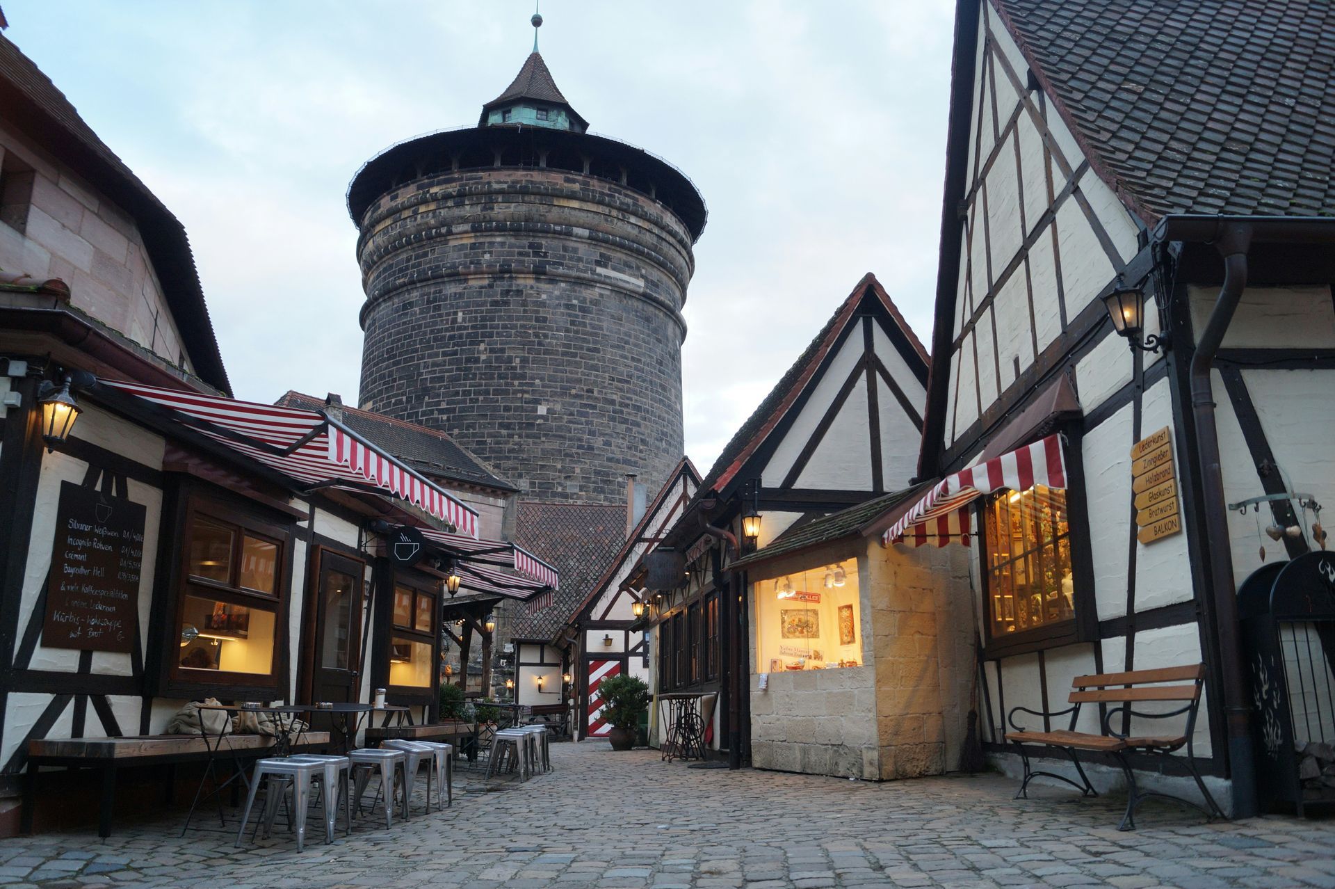 Stone tower in a narrow alley flanked by half-timbered buildings and cafes, cobblestone street in Nuremberg, Germany.