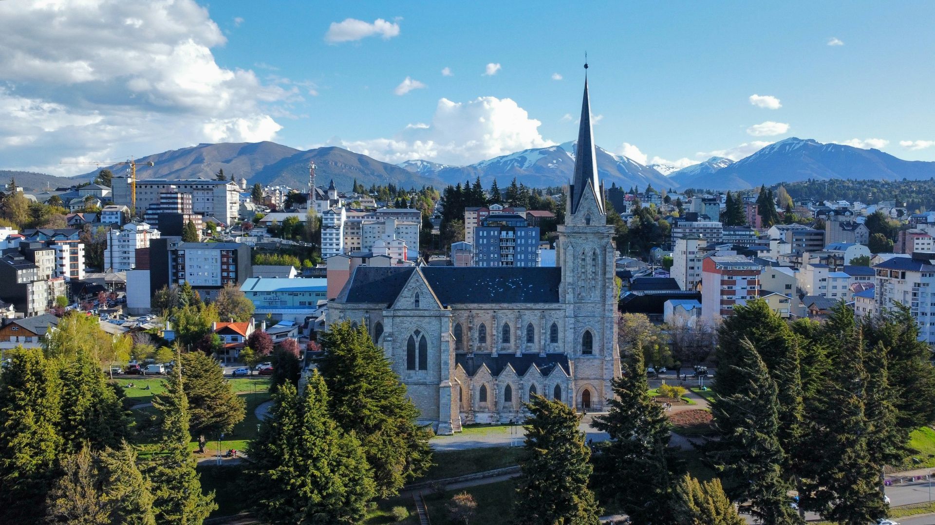 Bariloche Cathedral with tall spire, cityscape, mountains, and blue sky in San Carlos de Bariloche, Argentina.