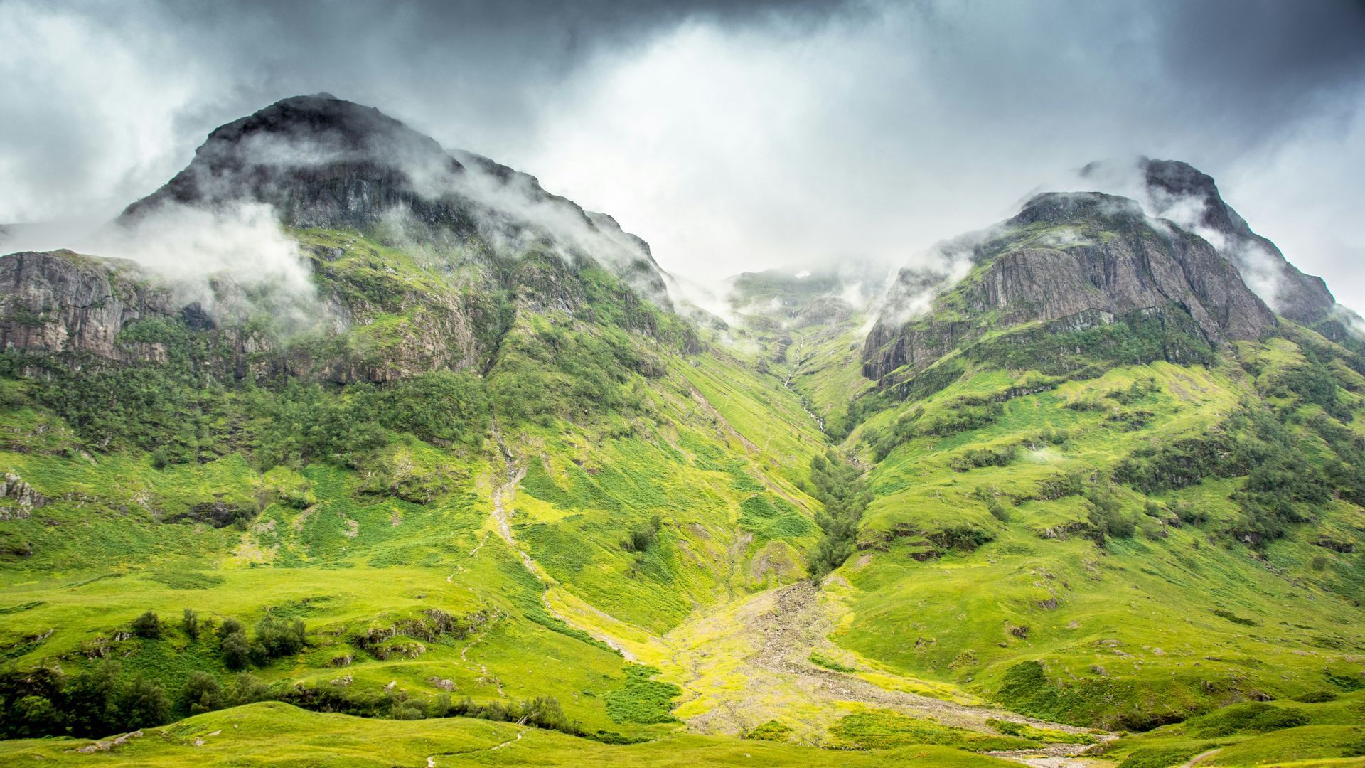 Green, rugged mountains shrouded in mist under a cloudy sky in Glencoe, Scotland.