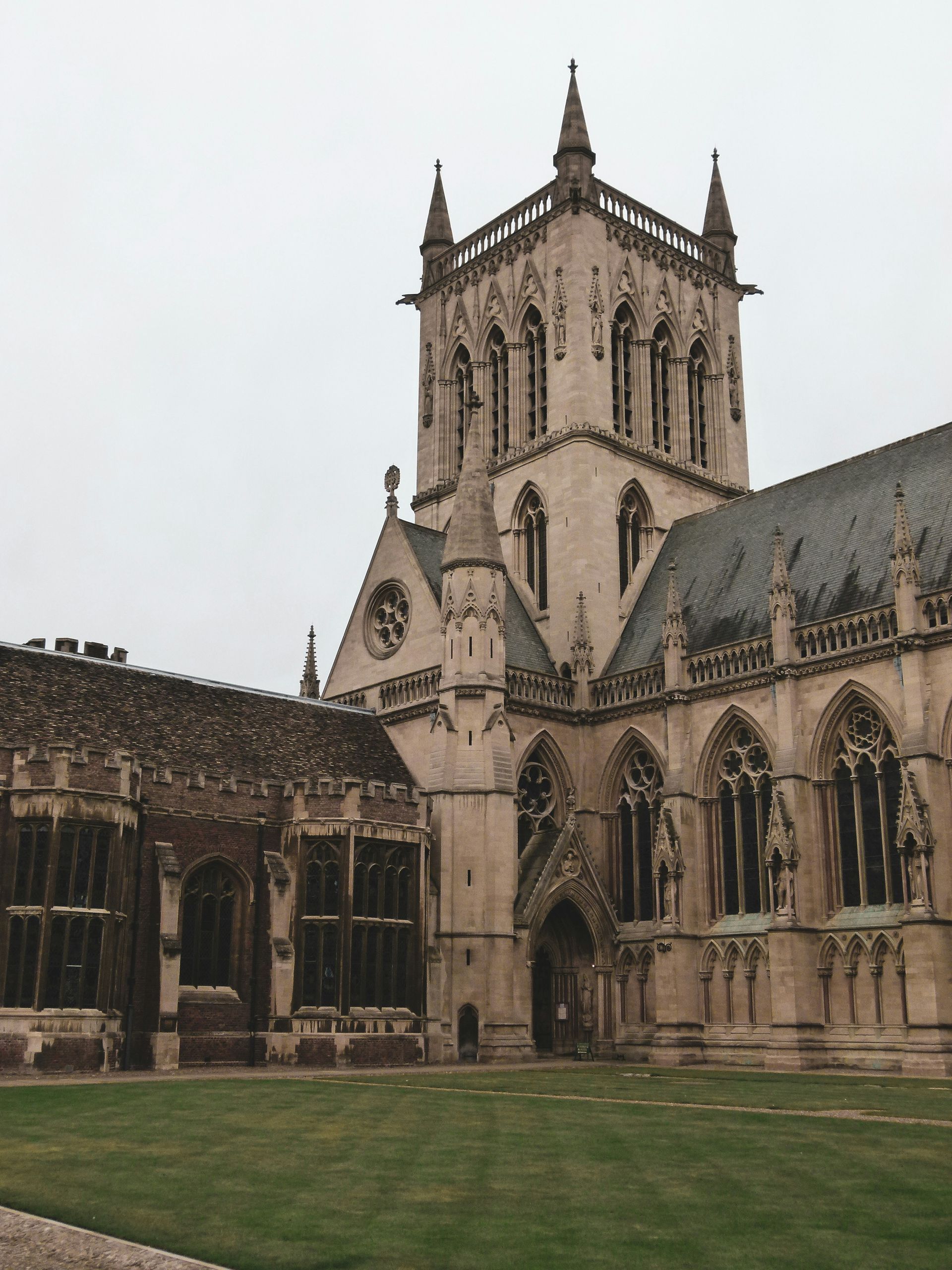 Gothic architecture cathedral. Beige stone facade, lawn in foreground, tower with spires at Oxford University, England.
