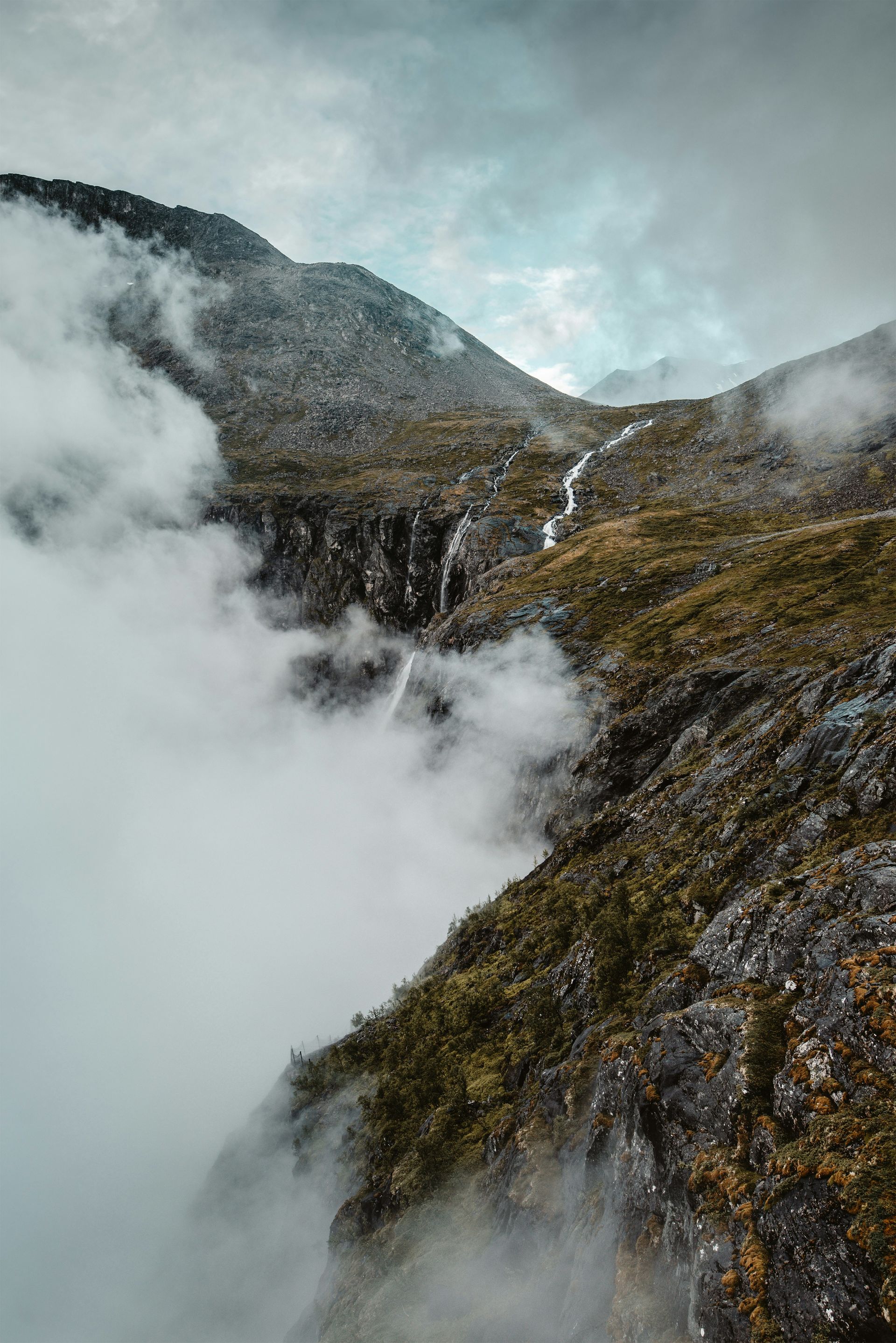 Mountain slope with waterfall, surrounded by fog in Jotunheimen National Park, Norway.