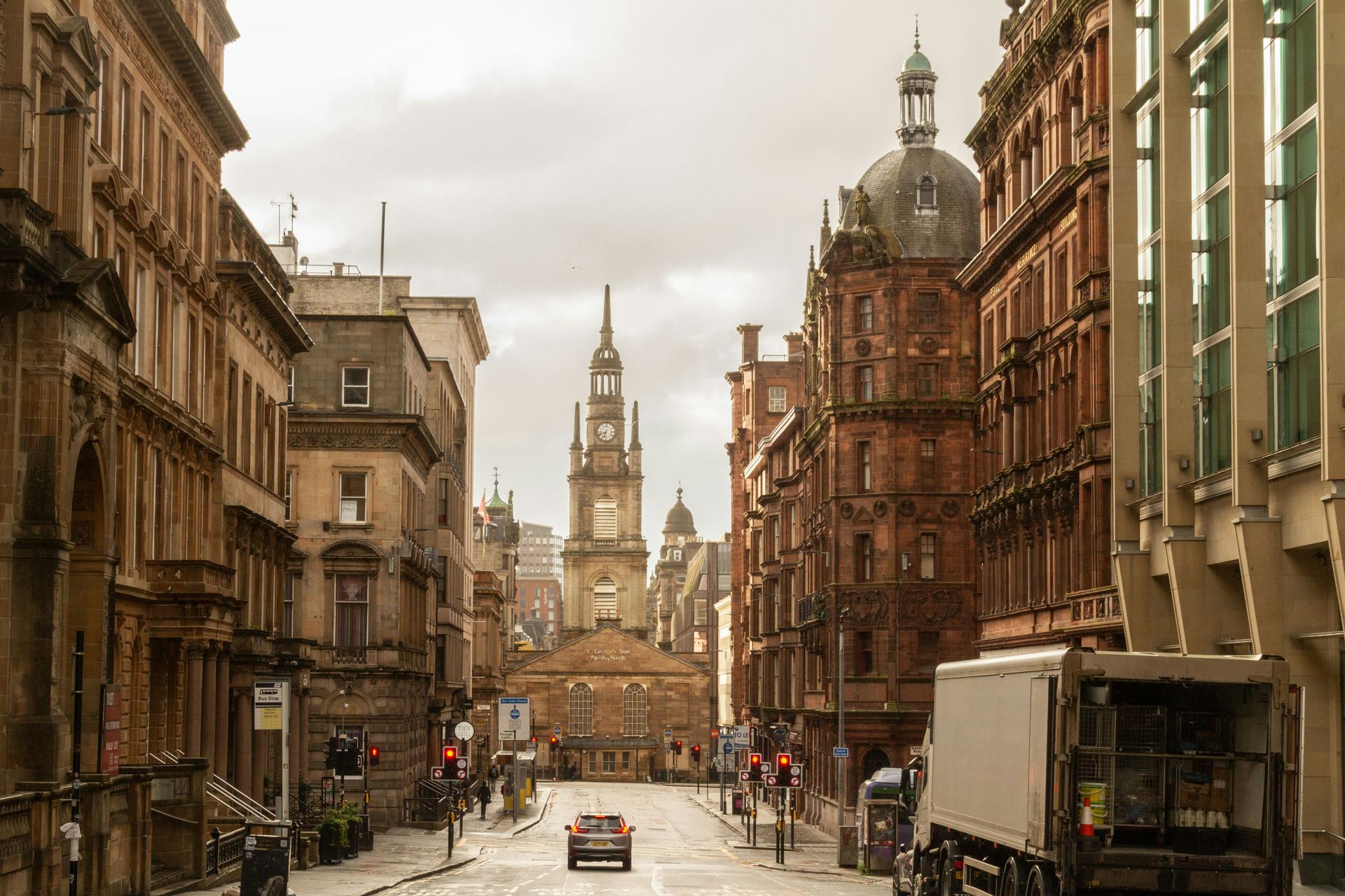 Street view of Glasgow with ornate buildings, a central steeple, and overcast skies.