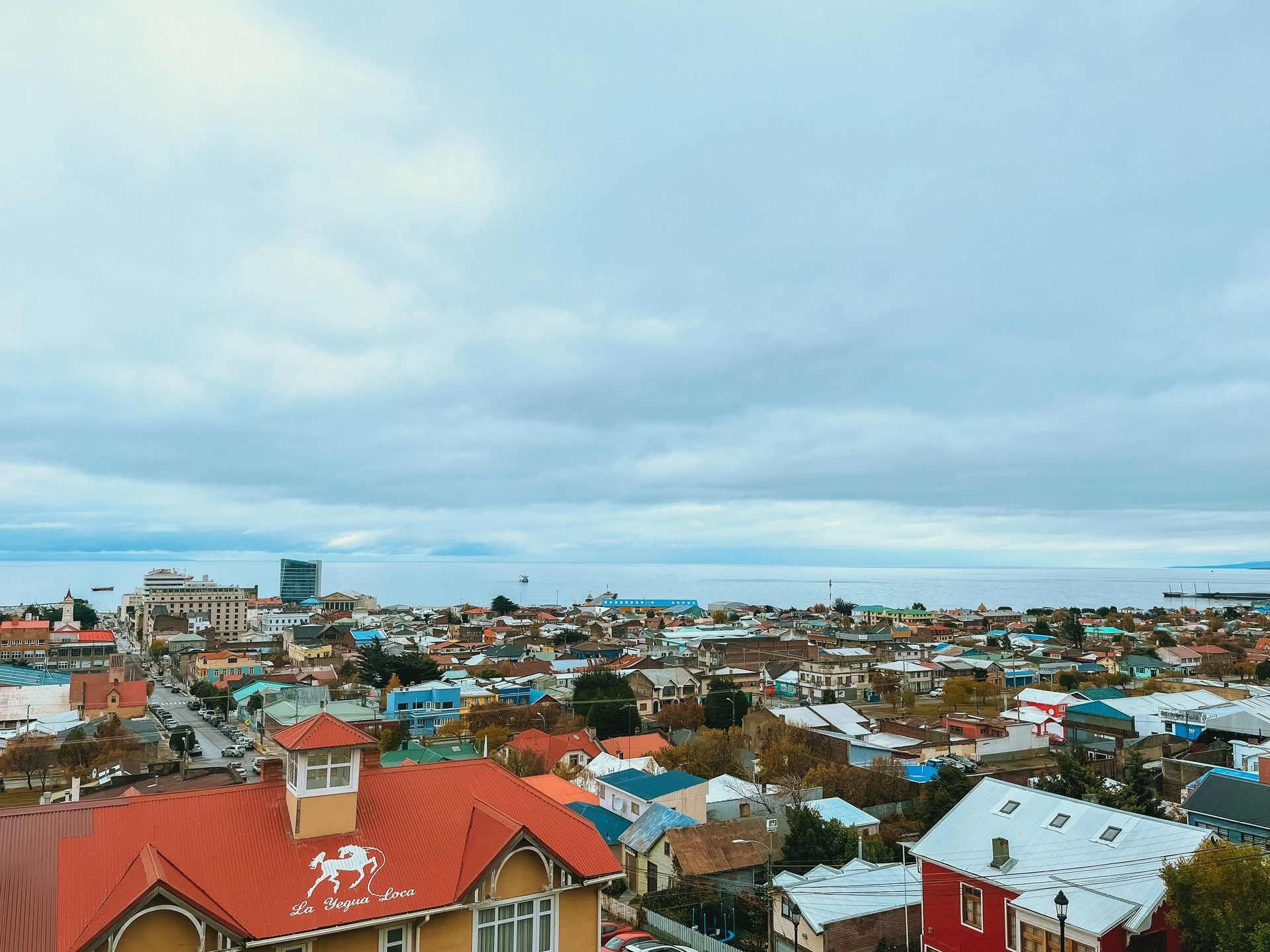Punta Arenas, Chile with colorful houses under a cloudy sky, overlooking a body of water.