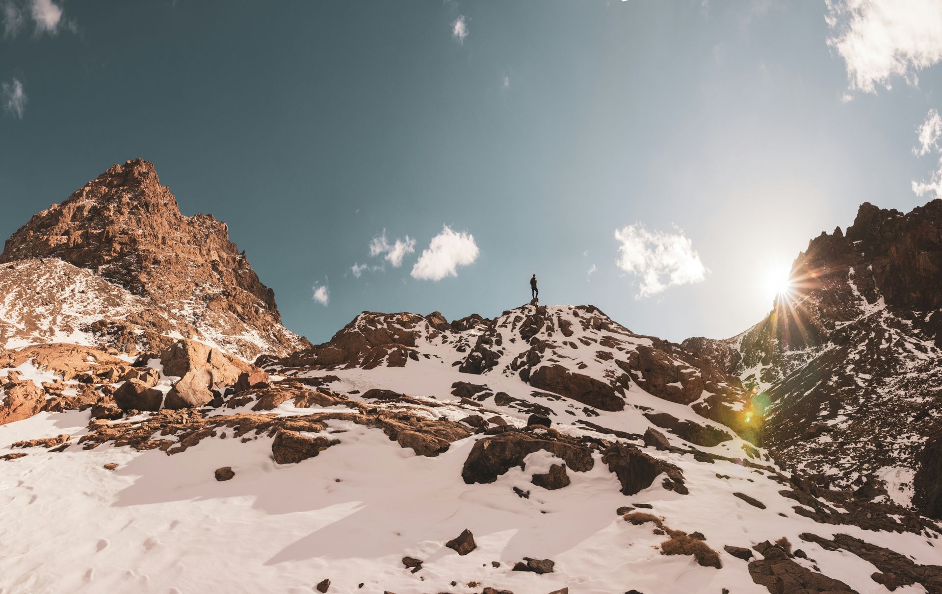 A person is standing on top of a snow covered mountain in Toubkal, Morocco.