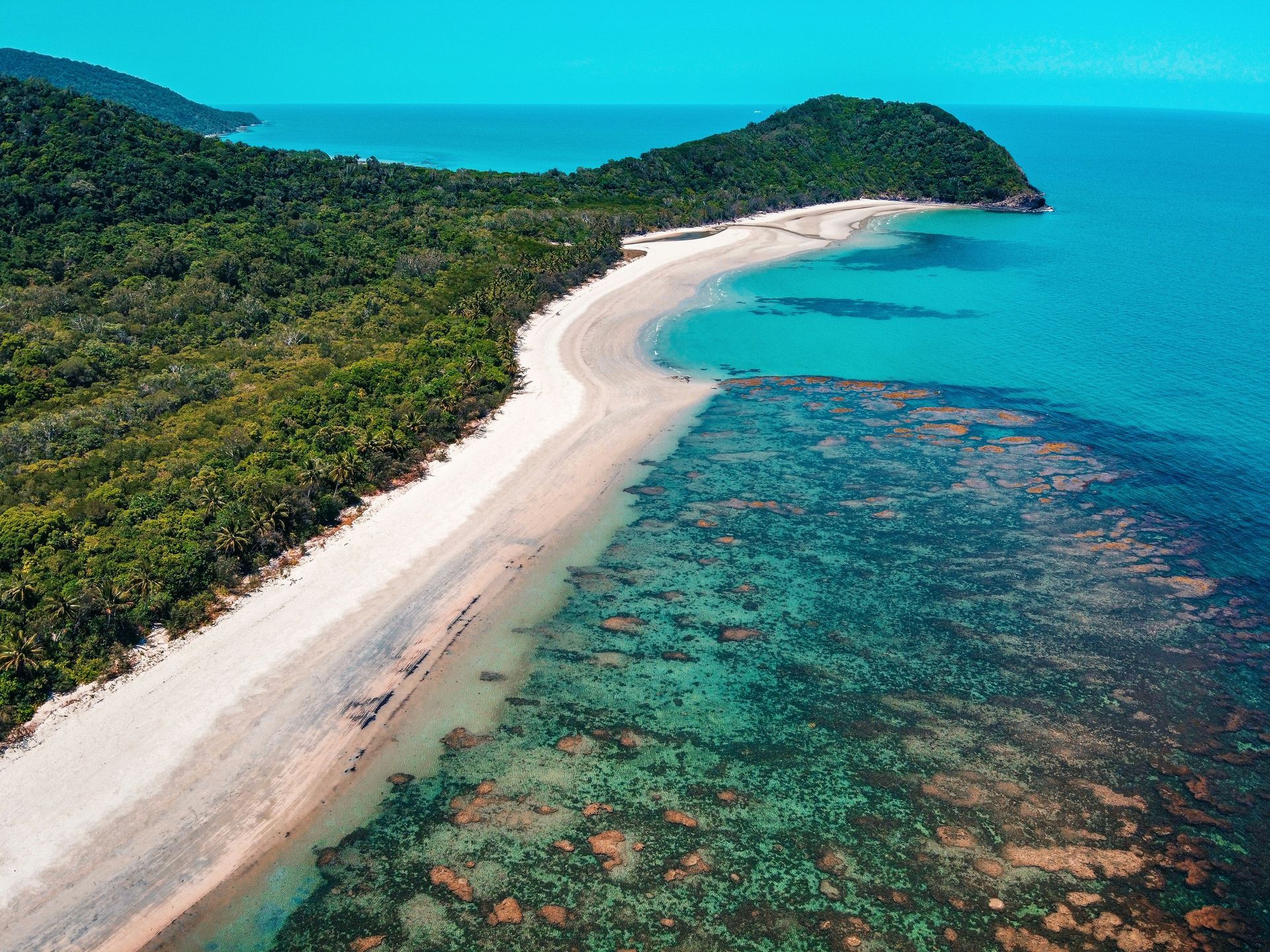 An aerial view of a beach with a coral reef and the Daintree Rainforest in the background in Australia.