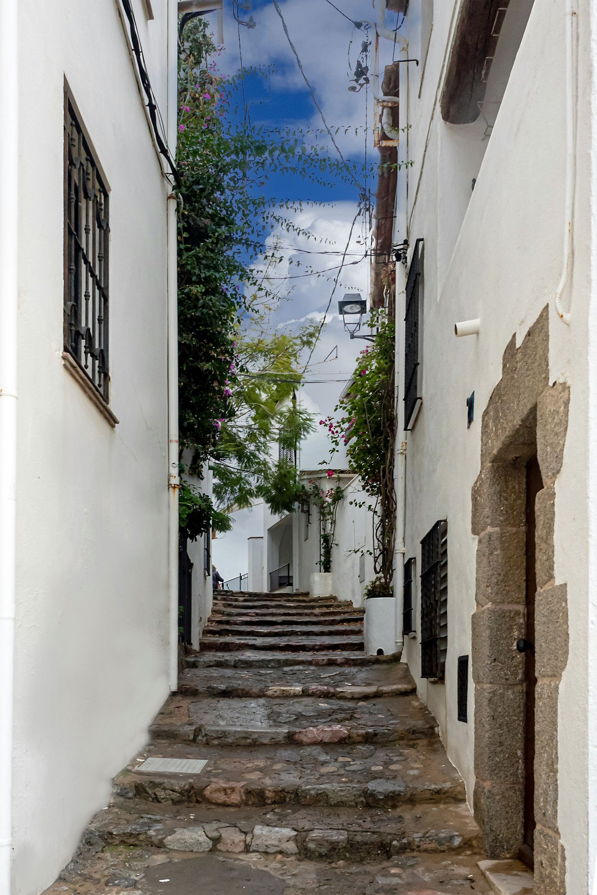 Narrow stone steps leading up a white-walled alleyway, blue sky above on Costa Brava, Spain.