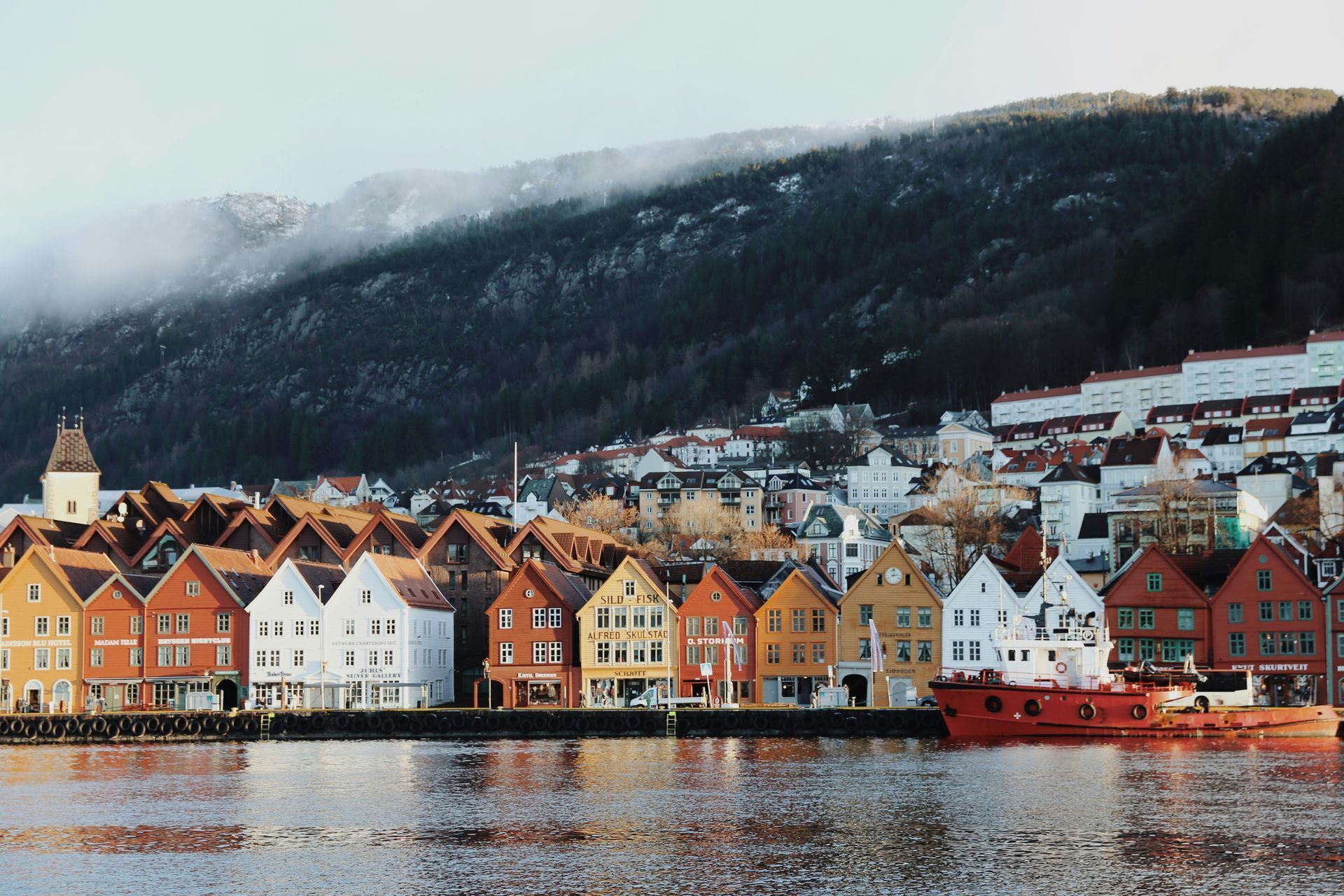 Colorful buildings line the waterfront in Bergen, Norway, with a snow-dusted mountain in the background.