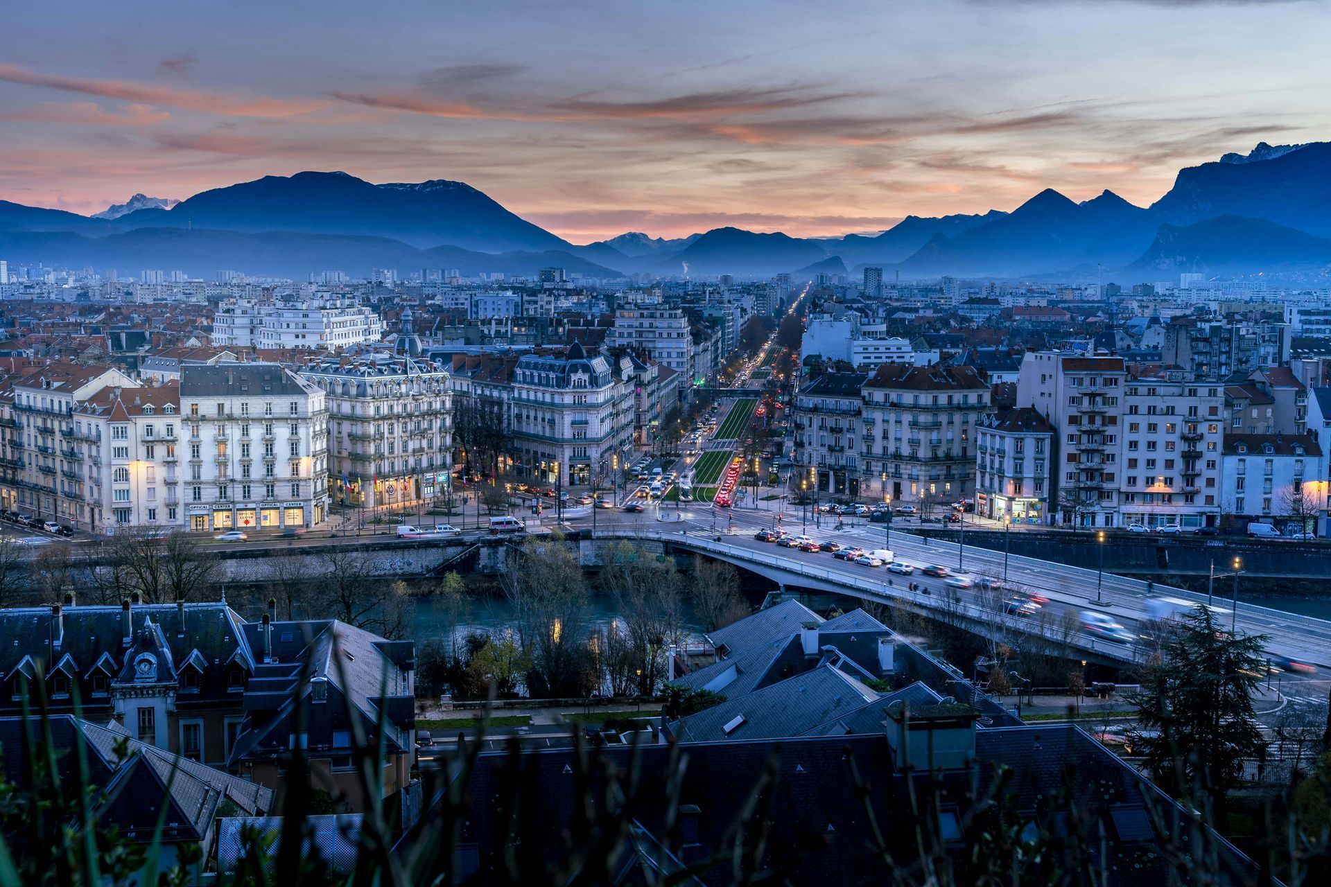An aerial view of Grenoble, France at night with mountains in the background.