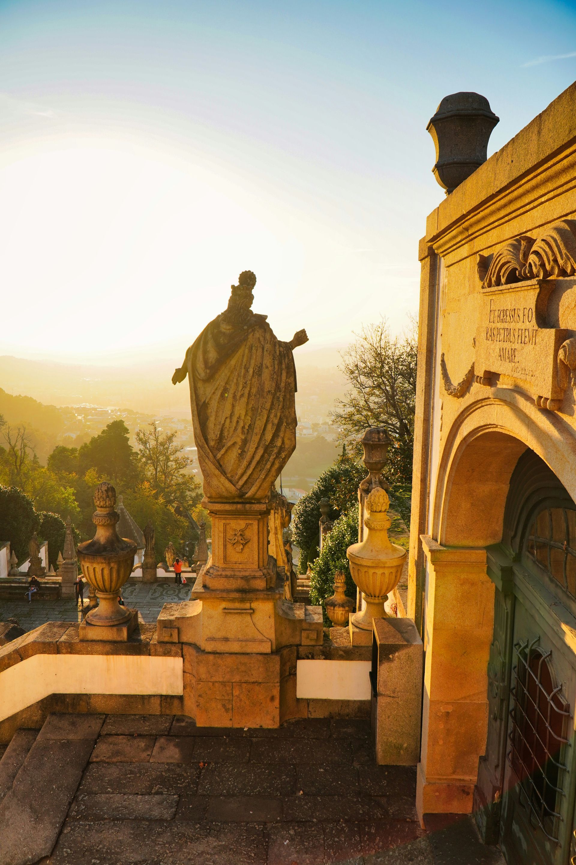 Stone statue atop a staircase, bathed in golden sunlight, overlooking Braga, Portugal.