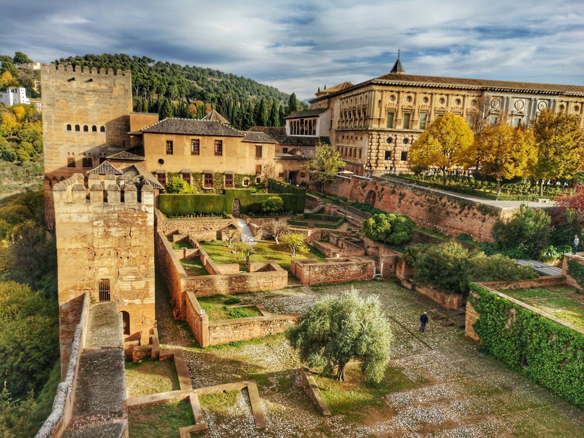 Historic fortress of Alhambra, Spain. Stone towers and buildings with gardens, under a cloudy sky.