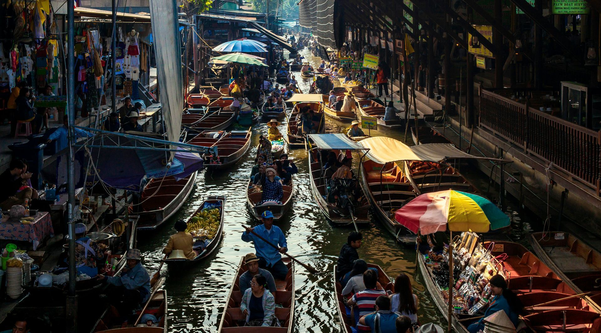 A group of people are riding boats down the Damnoen Saduak river market in Thailand.