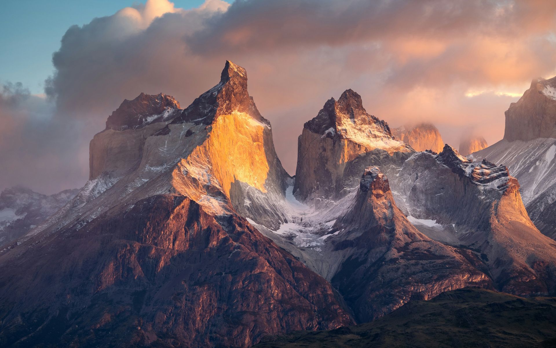 Snow-capped mountains peak as golden sunlight kisses their tops in Torres del Paine, Chile.
