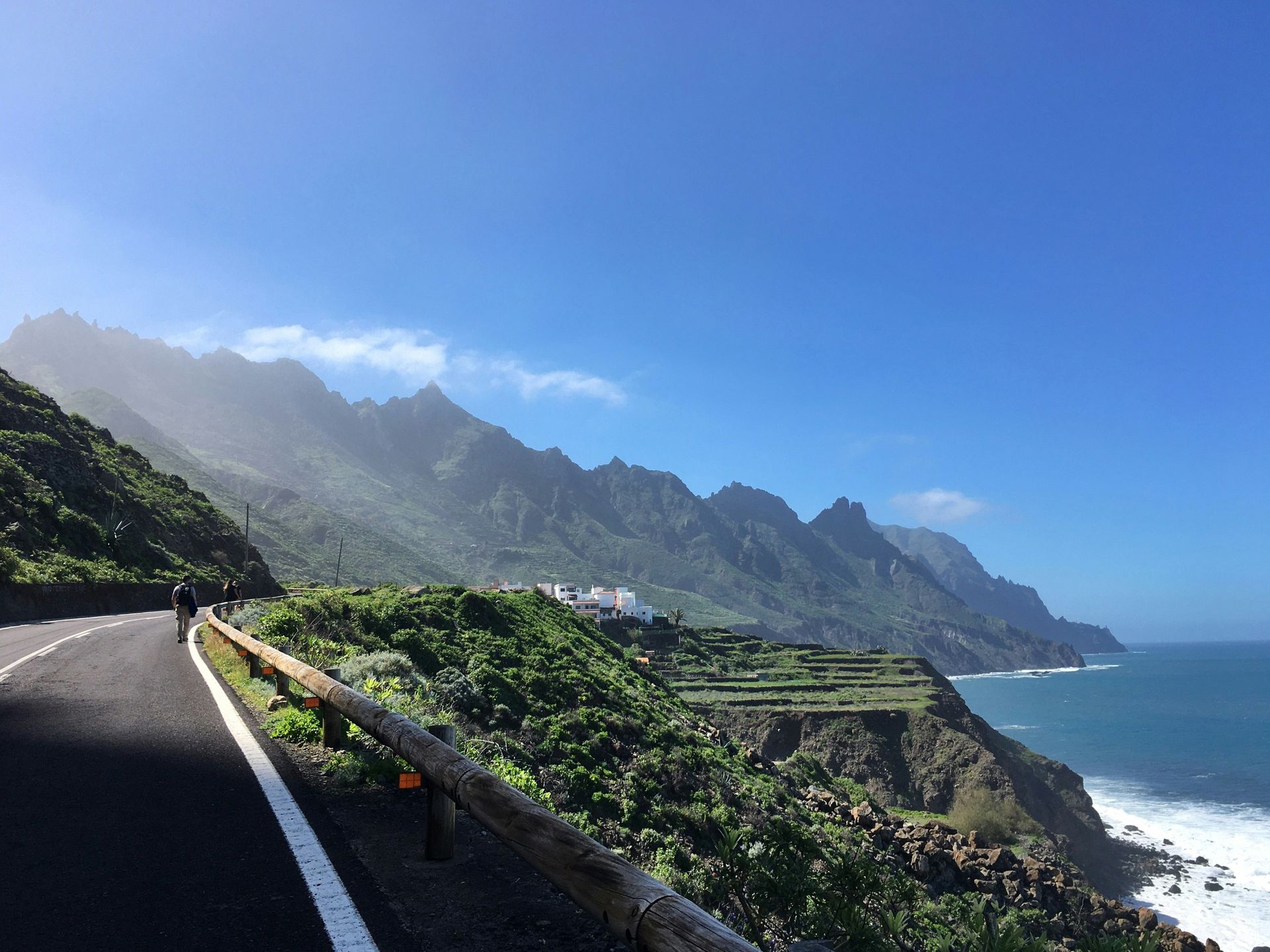 A winding road along a coast with mountains and the ocean under a clear blue sky on the Canary Islands, Spain.