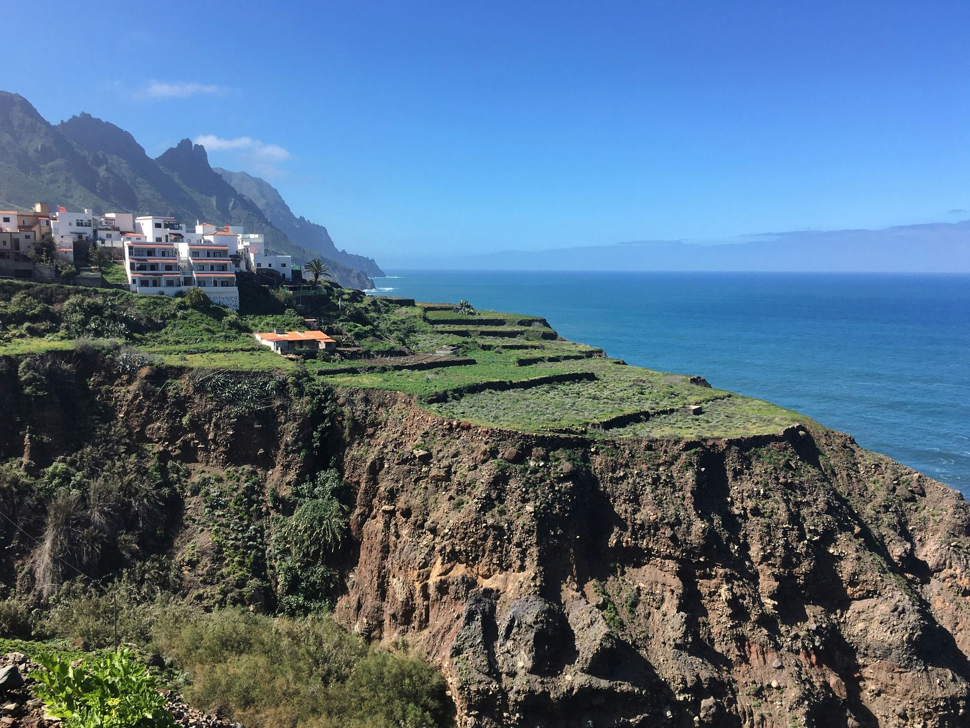 Cliffside village with terraced fields, turquoise ocean, mountains on the Canary Islands, Spain.
