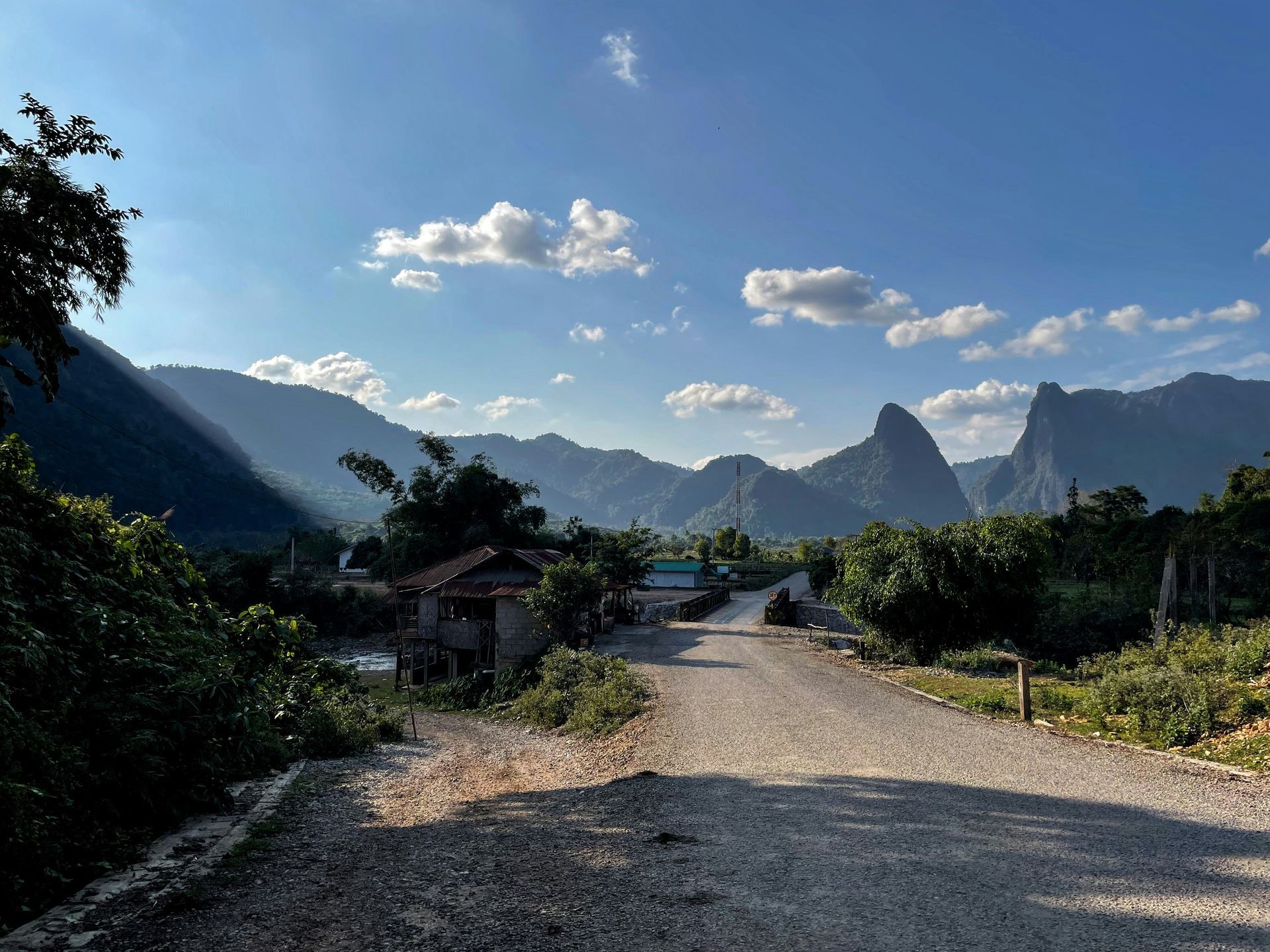 Gravel road leading to a mountainous landscape. Small buildings and trees line the road in Vang Vieng, Laos.