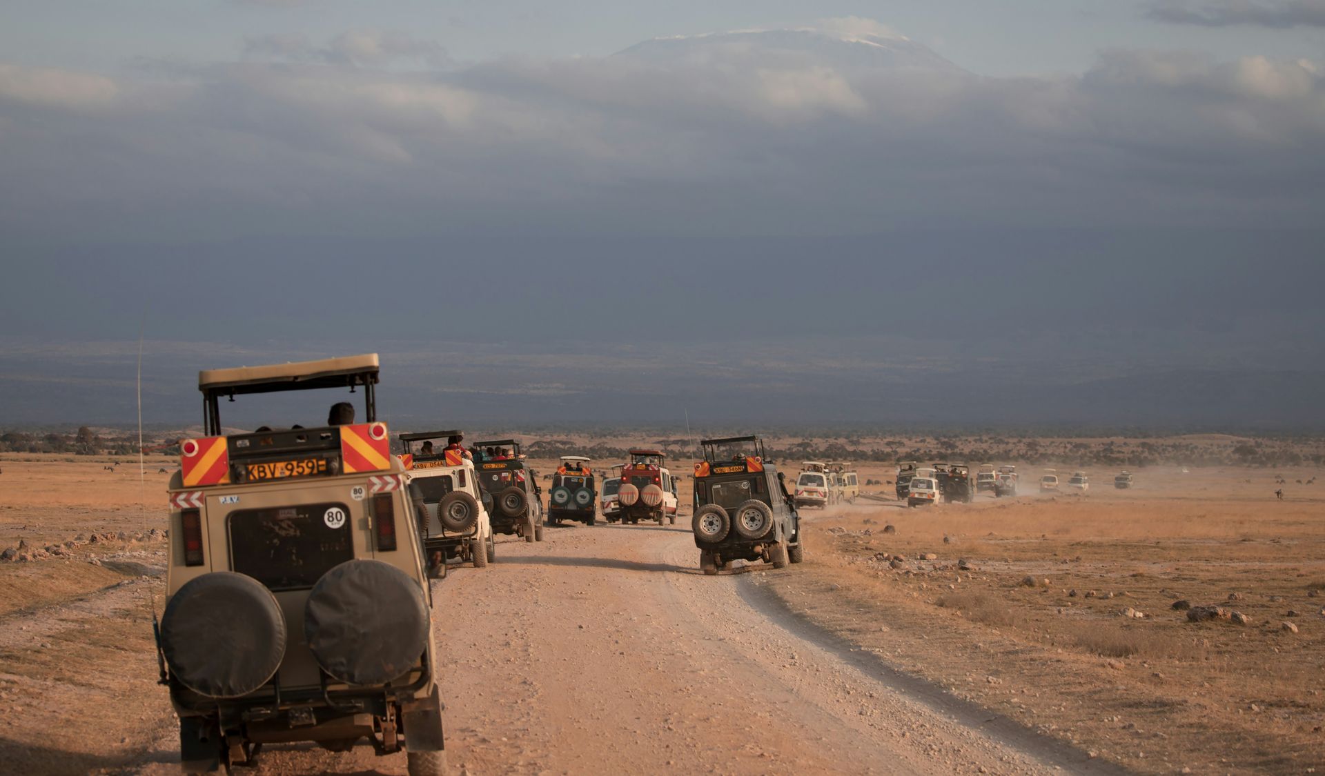 Safari vehicles driving on a dirt road in an open landscape in Amboseli National Park, Kenya.
