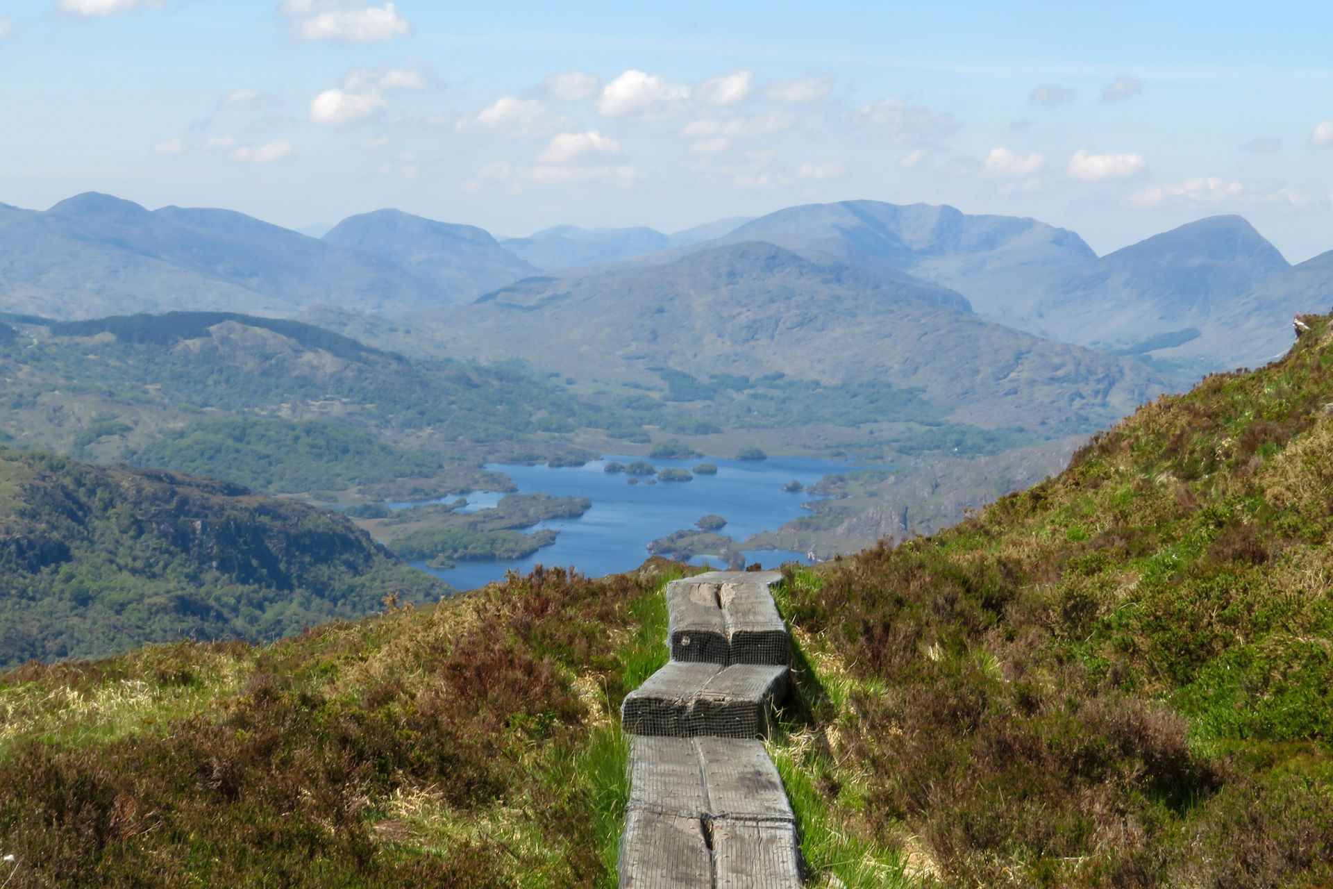 Wooden walkway overlooking a lake and mountains under a blue sky in Killarney, Ireland.