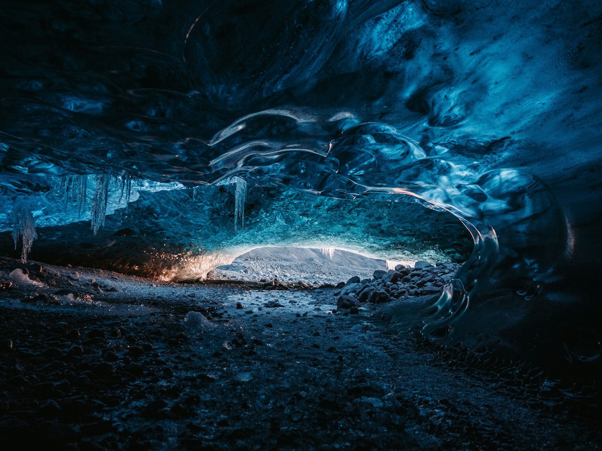 Inside a glacial ice cave, blue-tinted ice glows, a brighter opening in the distance at Jökulsárlón Glacier Lagoon, Iceland.