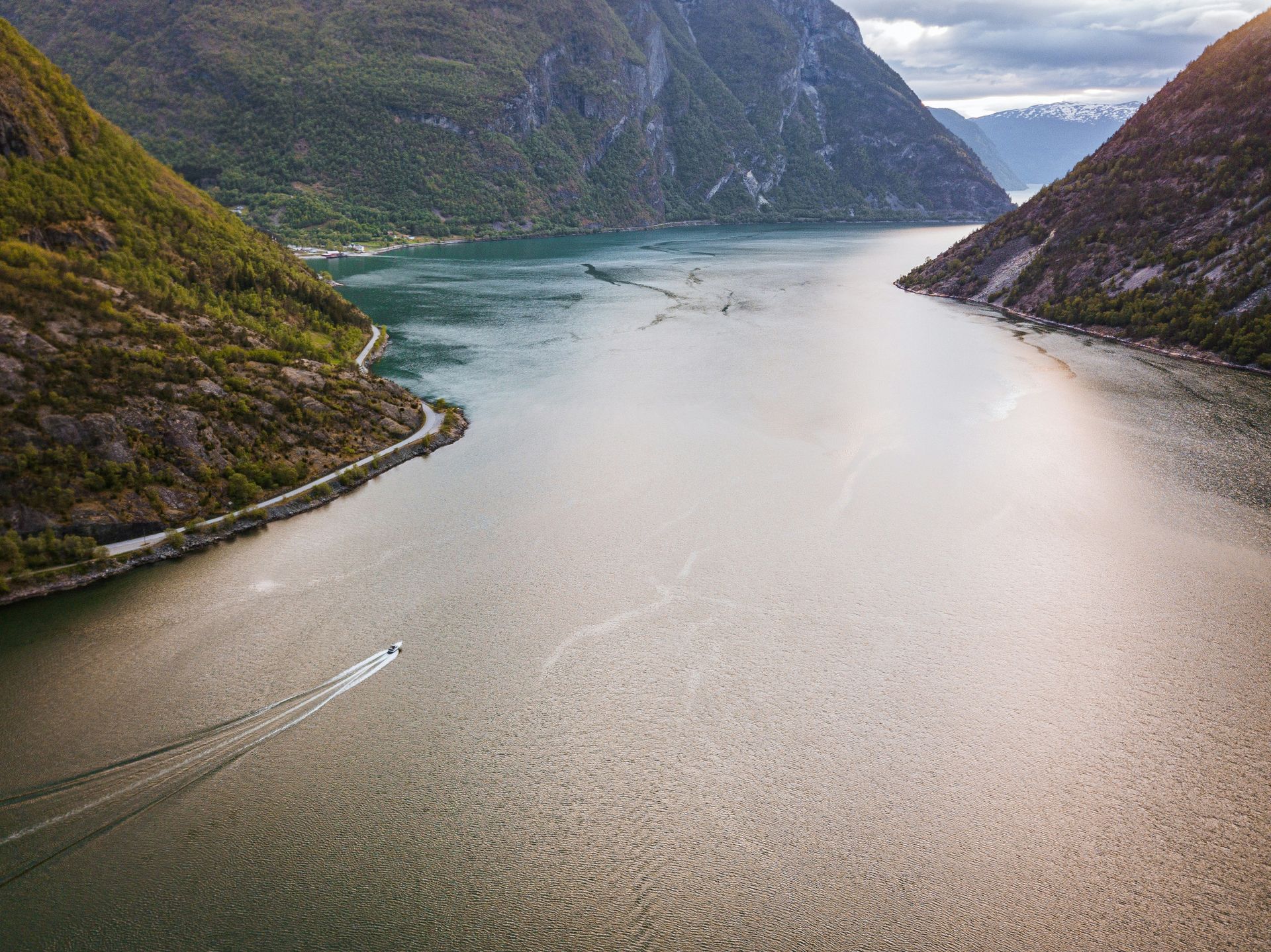 Boat sailing on the Sognefjord, flanked by green mountains and a road in Norway.
