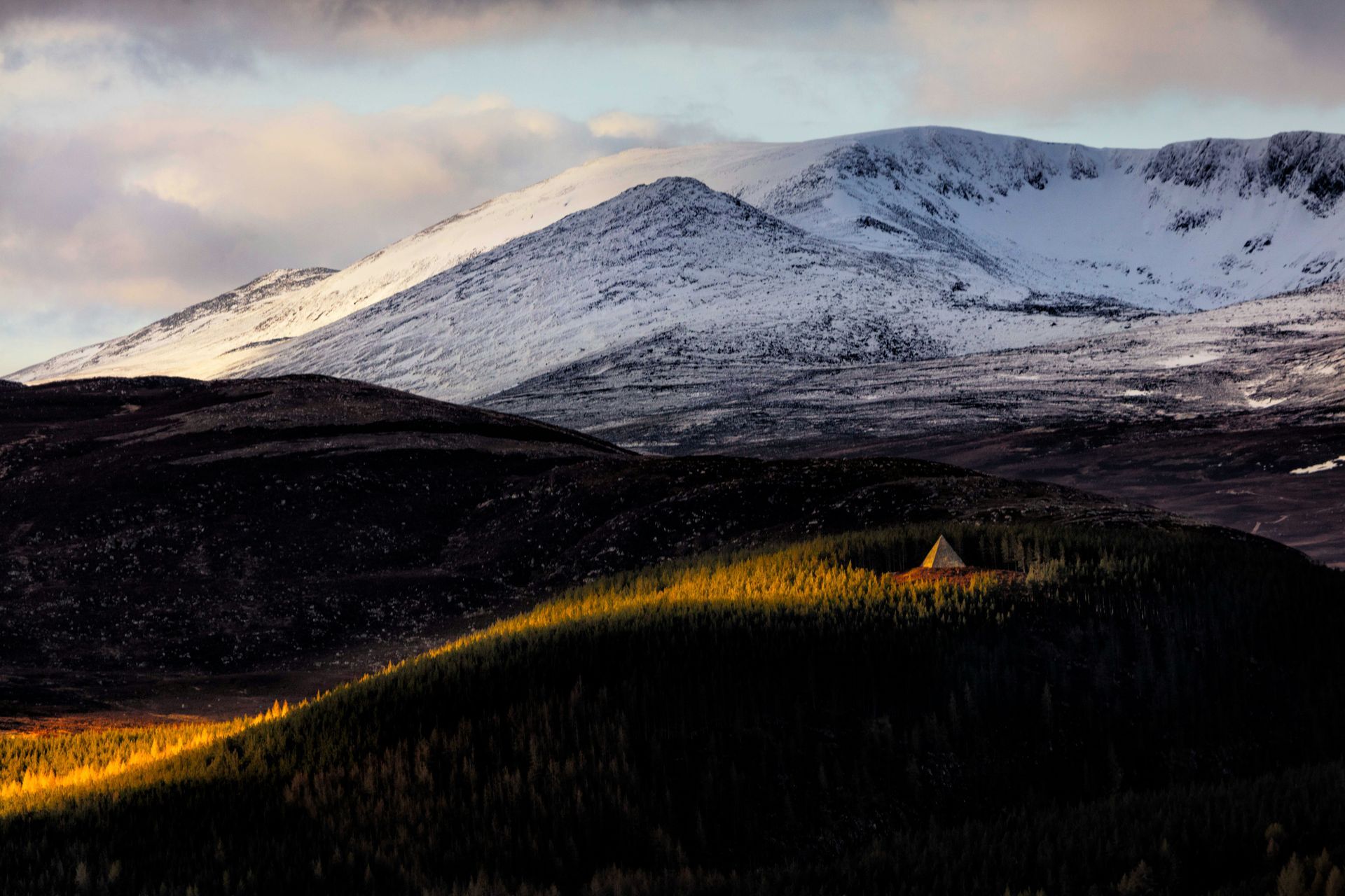 Snow-capped mountain range behind rolling hills and the Prince Albert Memorial Pyramid in the Cairngorms, Scotland.