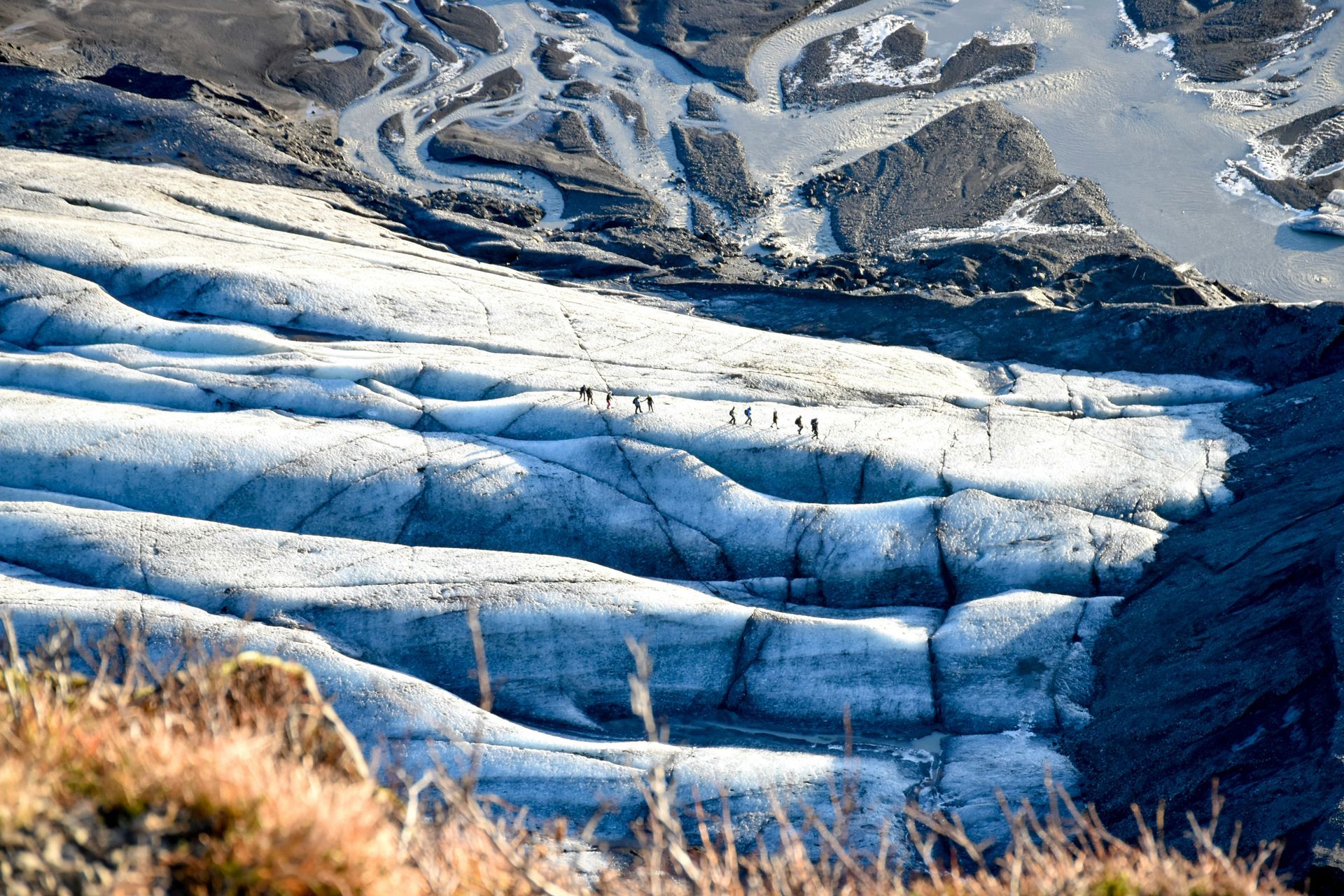 Glacier with visible crevasses and several tiny figures of people traversing it at Vatnajökull National Park, Iceland.