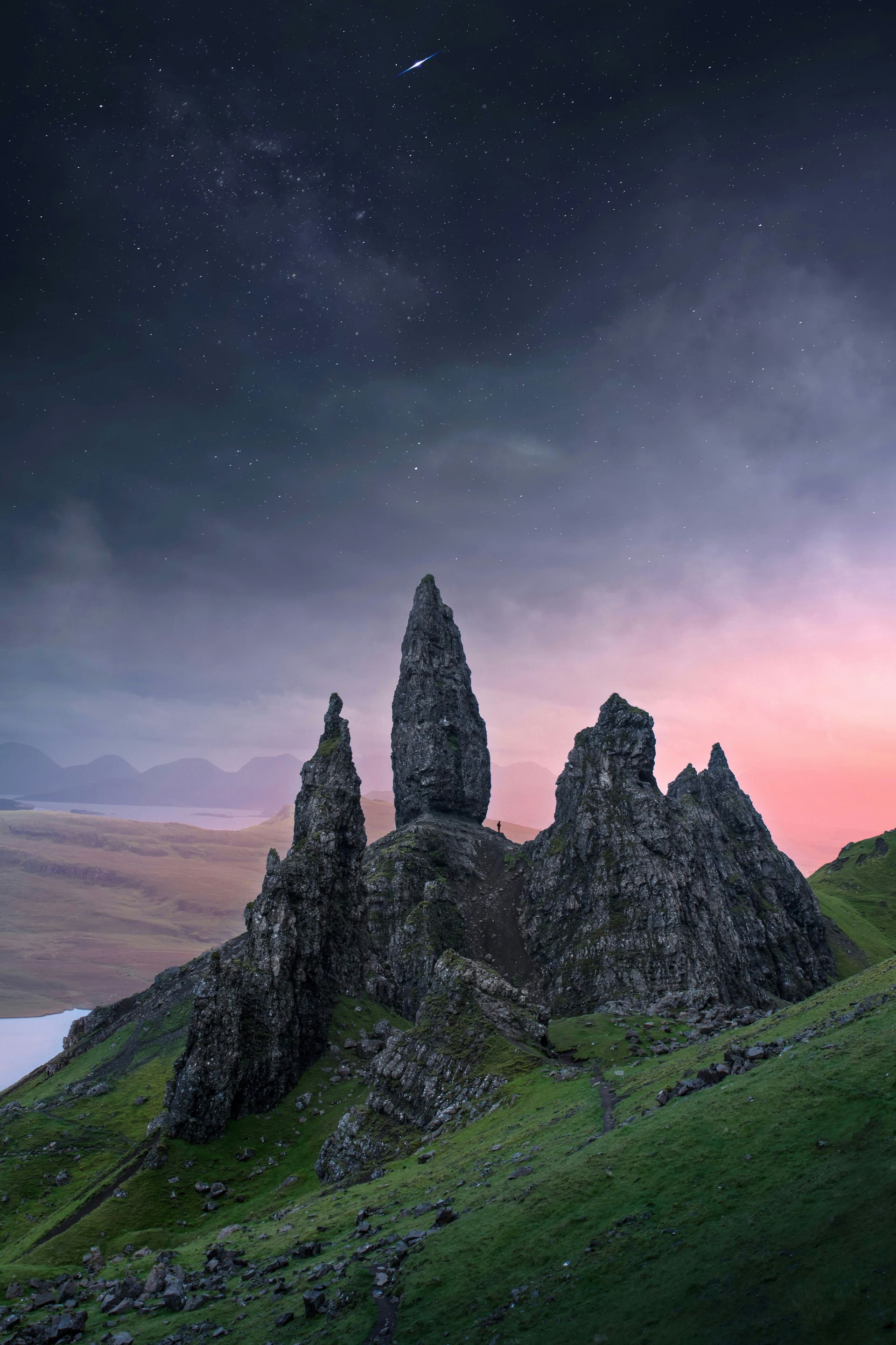 The Storr mountain's rock formations on a green hillside under a starry sky at sunset on the Isle of Skye, Scotland.