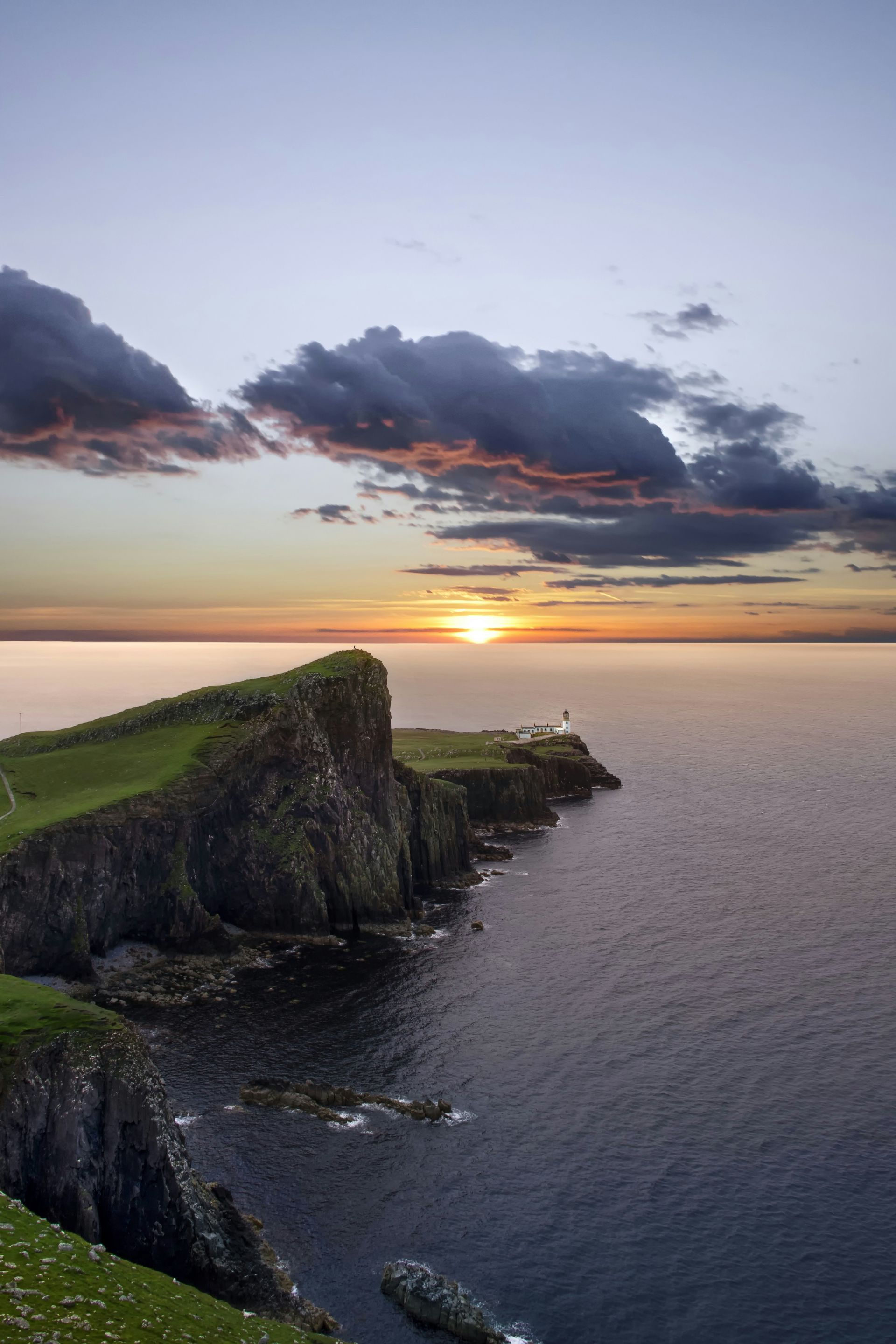 Sunset over a rugged coastline with a lighthouse, cliffs, and ocean on the Isle of Skye, Scotland.