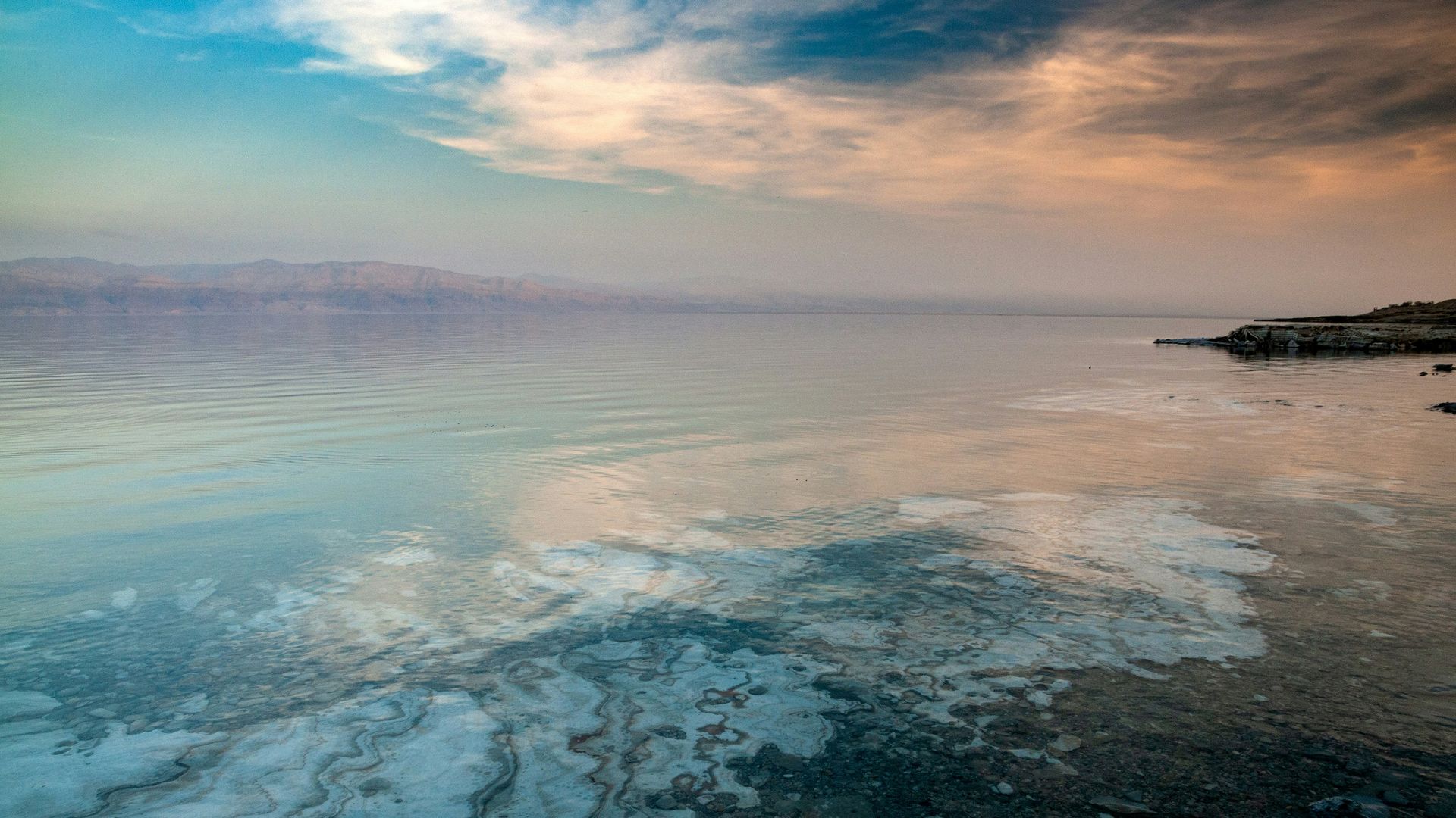 Dead Sea eflecting cloudy sky with a shoreline in the distance in Jordan.
