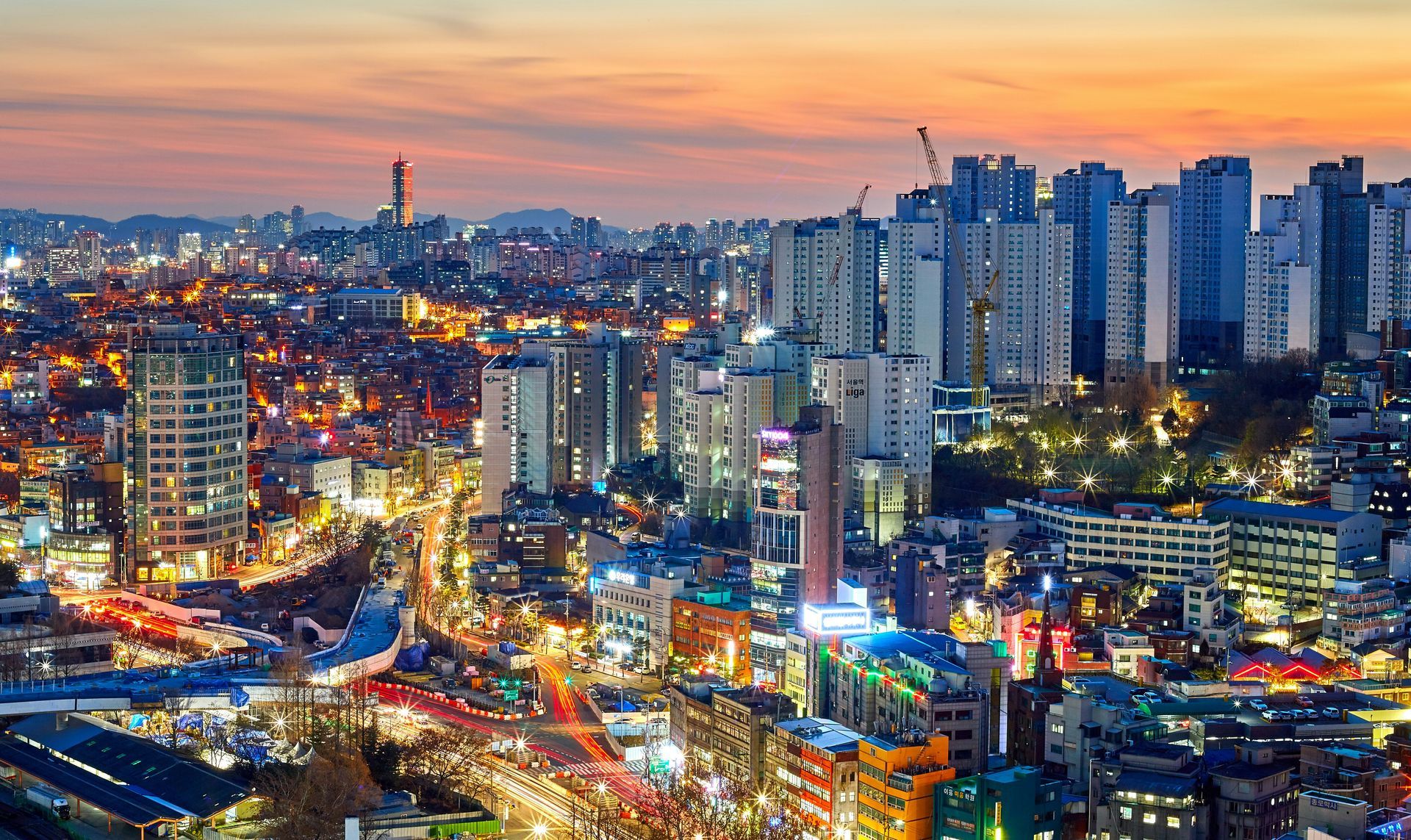 Seoul at dusk with illuminated buildings and roads. Orange and blue sky overhead in South Korea.