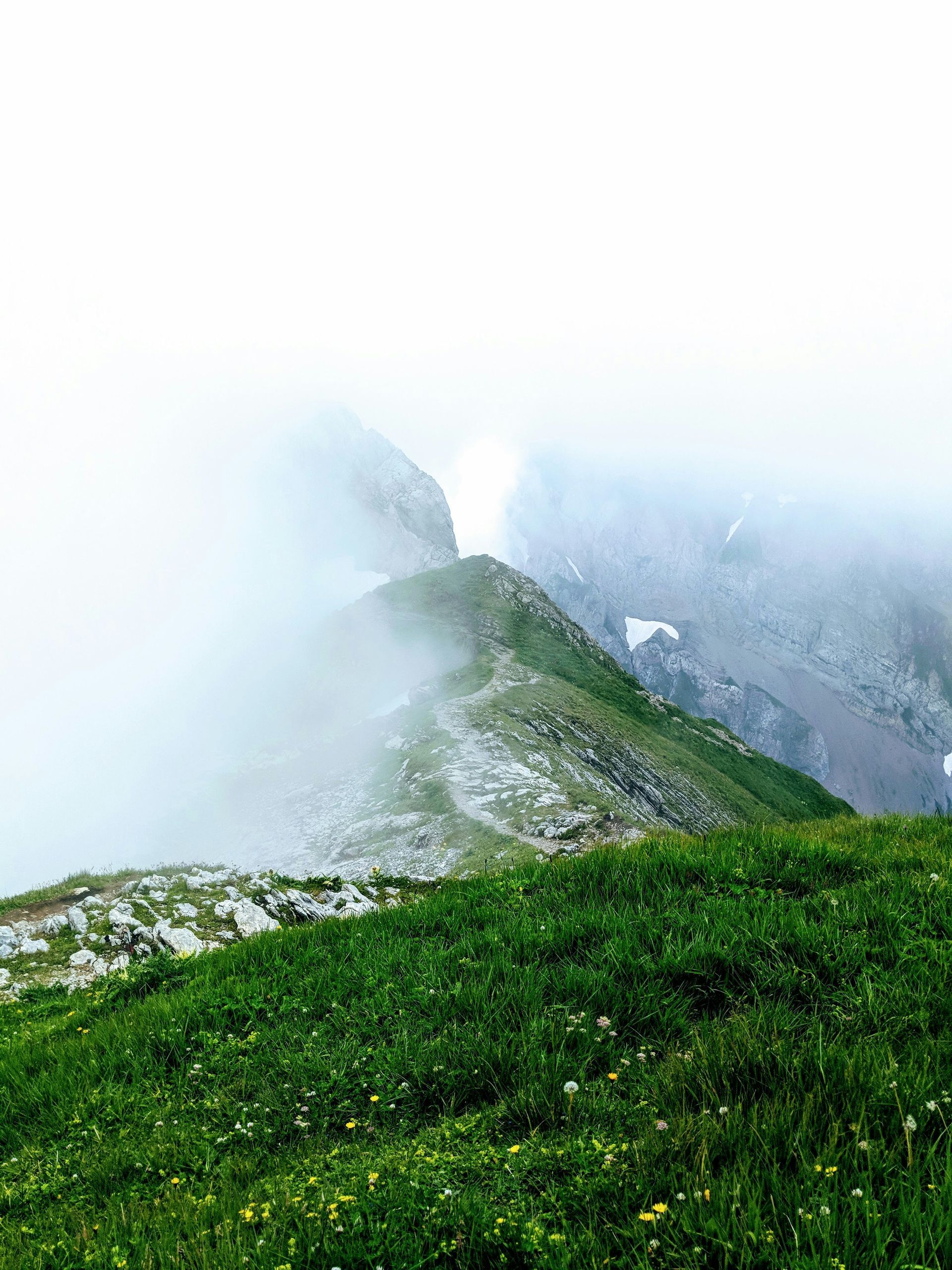 Green mountain ridge shrouded in mist, path leading toward distant peaks in Seealpsee, Switzerland.