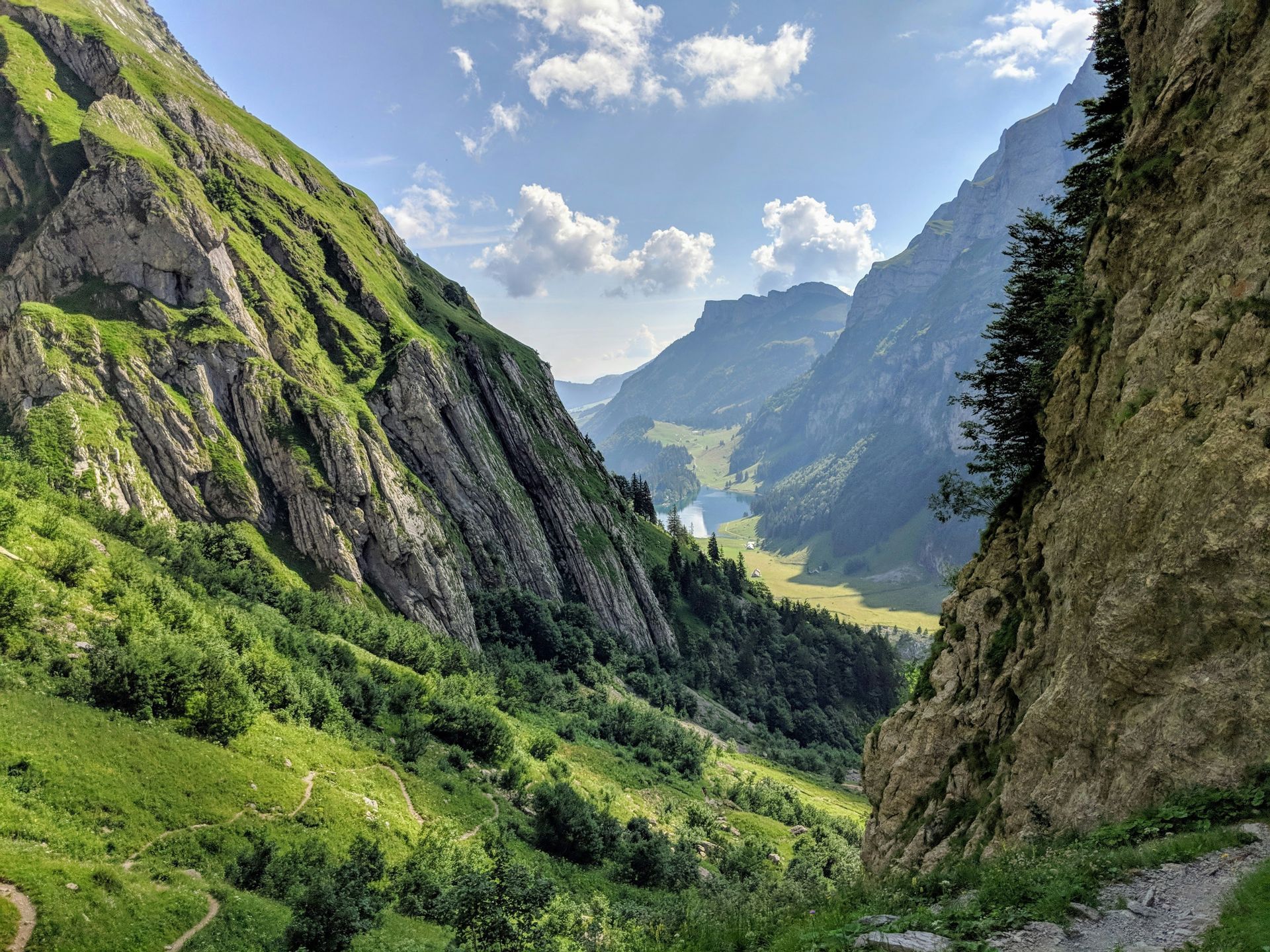 Green mountain valley with a lake, under a blue sky with fluffy white clouds in Seealpsee, Switzerland.