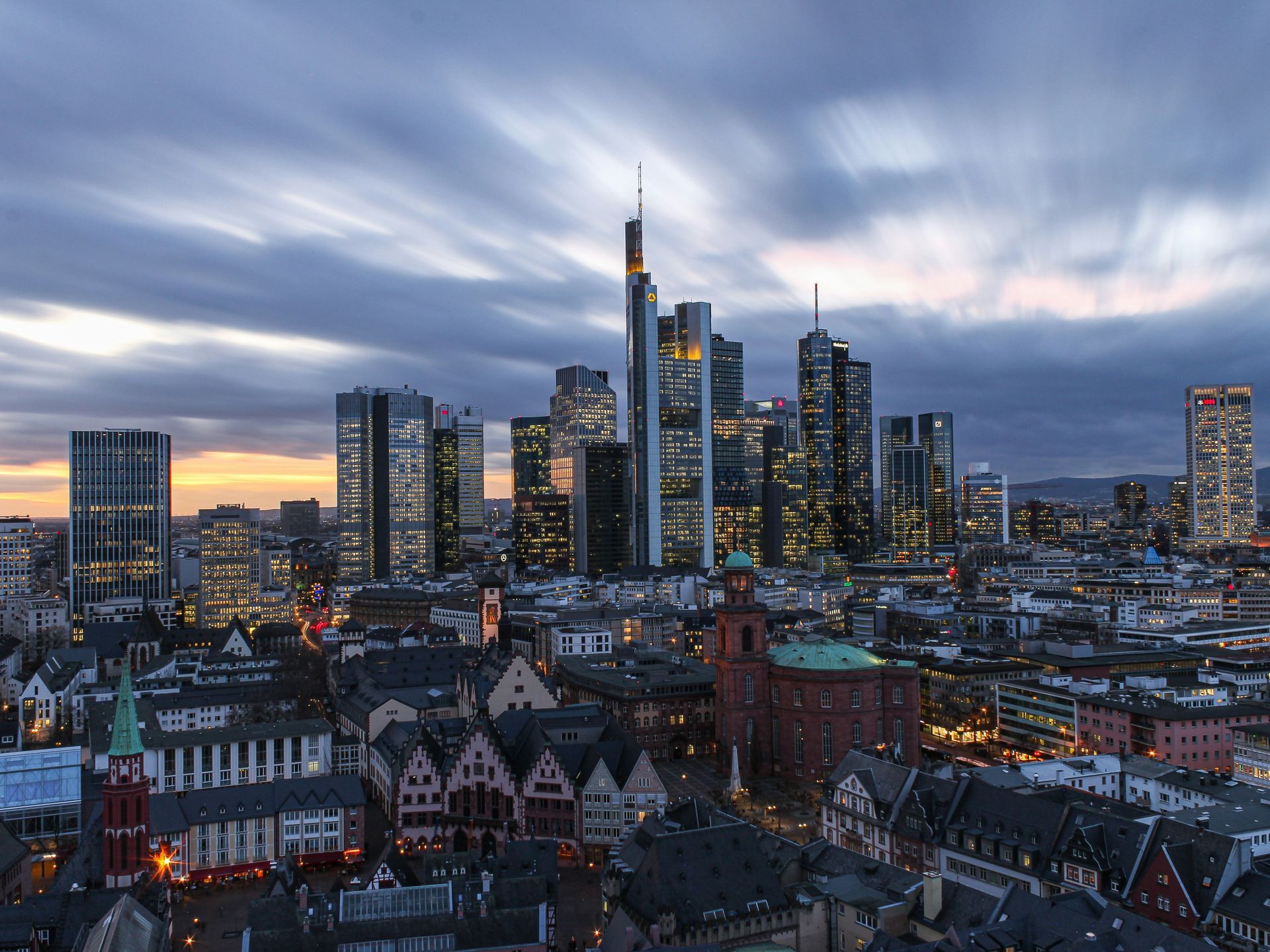 Frankfurt skyline at dusk, featuring skyscrapers and historic buildings under a cloudy sky.