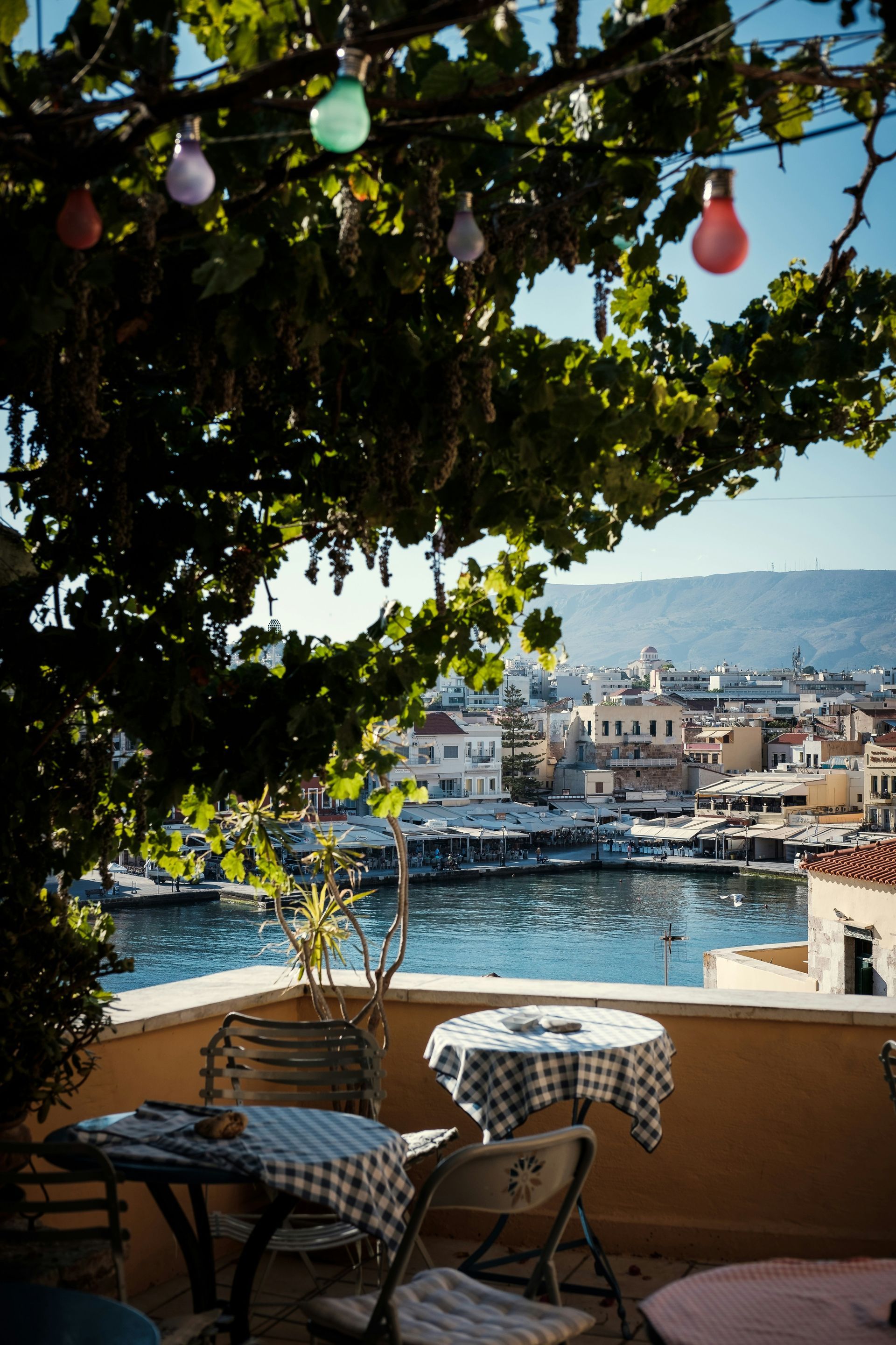 A table and chairs under a tree overlooking a body of water in Crete, Greece.