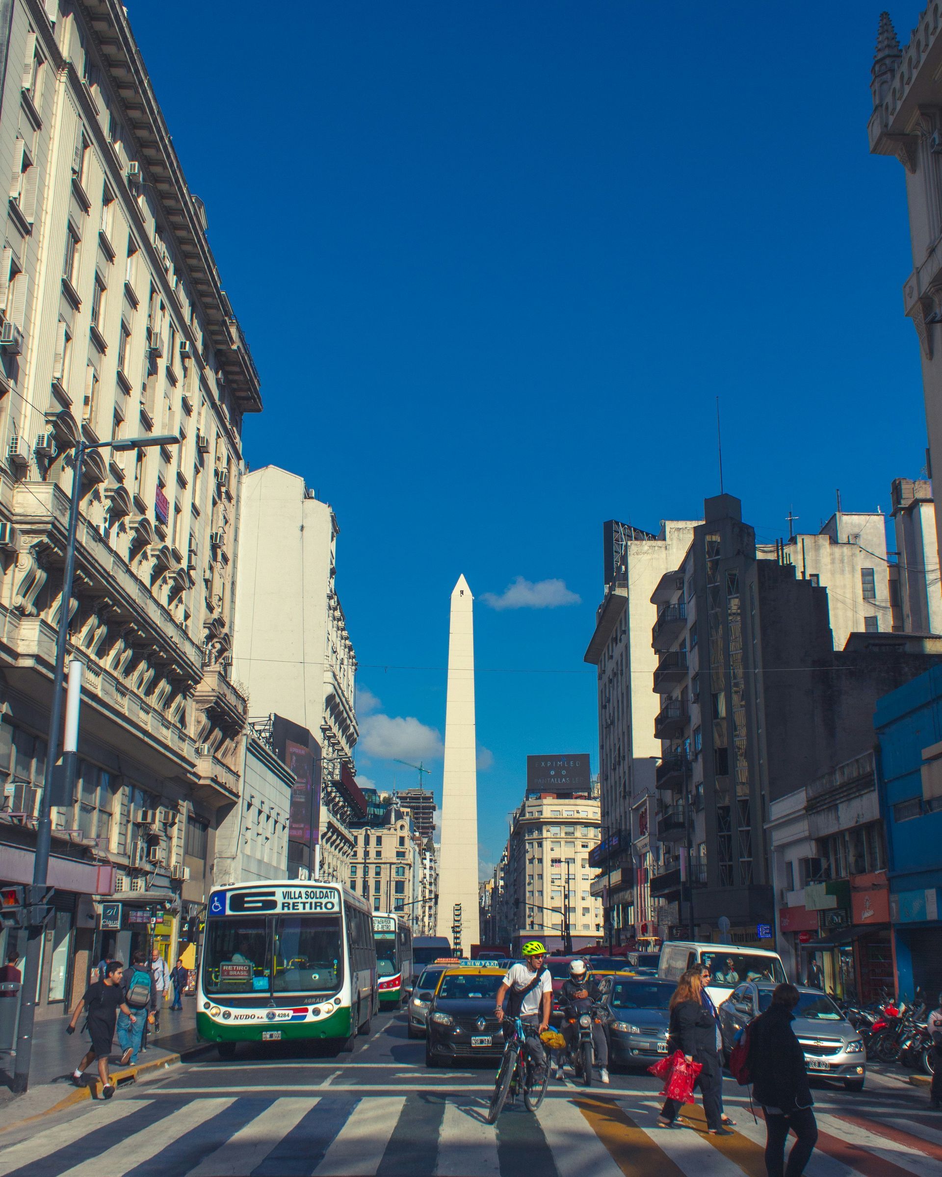 Obelisco de Buenos Aires in Argentina, seen down a busy street, blue sky above.