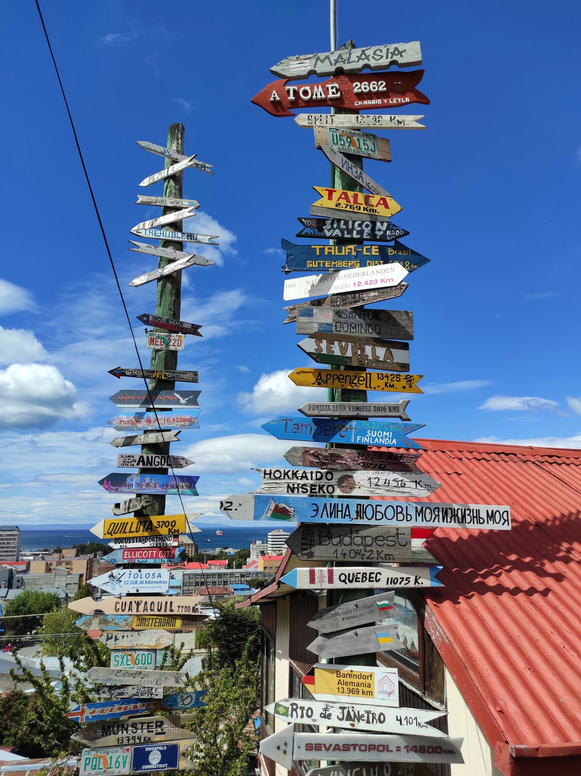 A tall signpost covered in directional signs; colorful, in an urban setting in Punta Arenas, Chile.