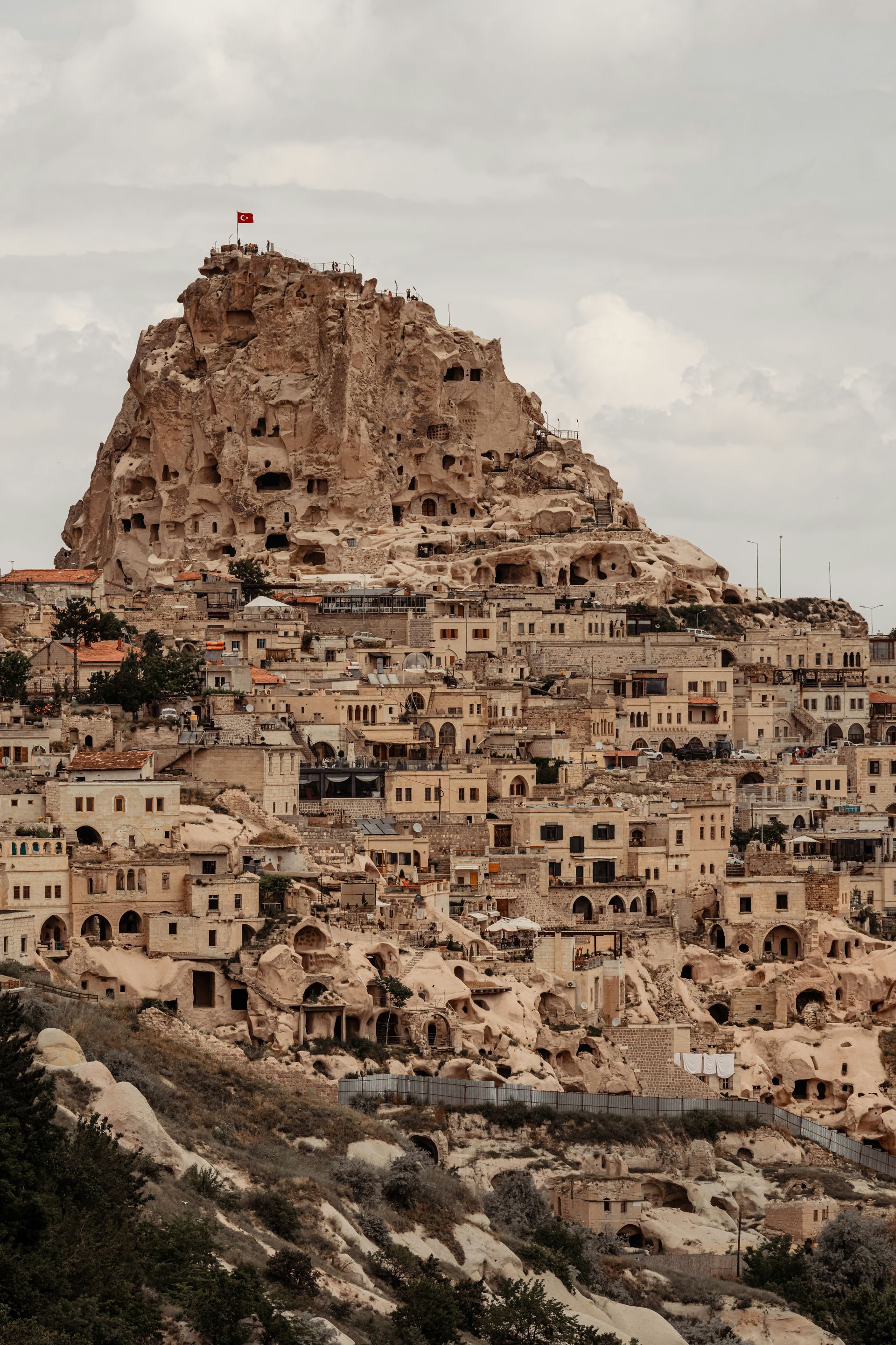 Uçhisar Castle in Cappadocia, Turkey, with houses built into the rock face and a flag atop the summit.