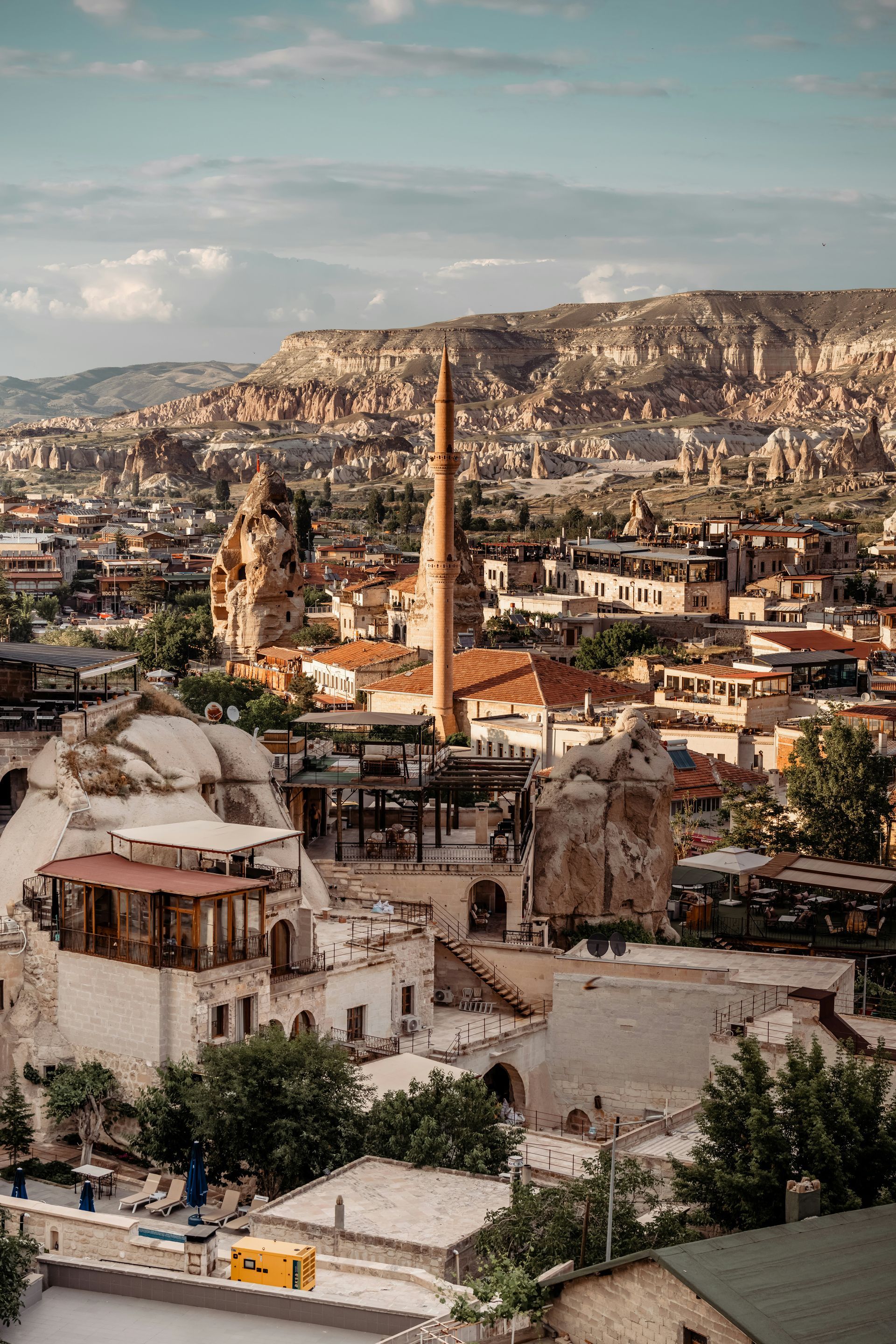 Cappadocia, Turkey cityscape. White buildings with orange roofs, tall minaret, and unique rock formations in background.